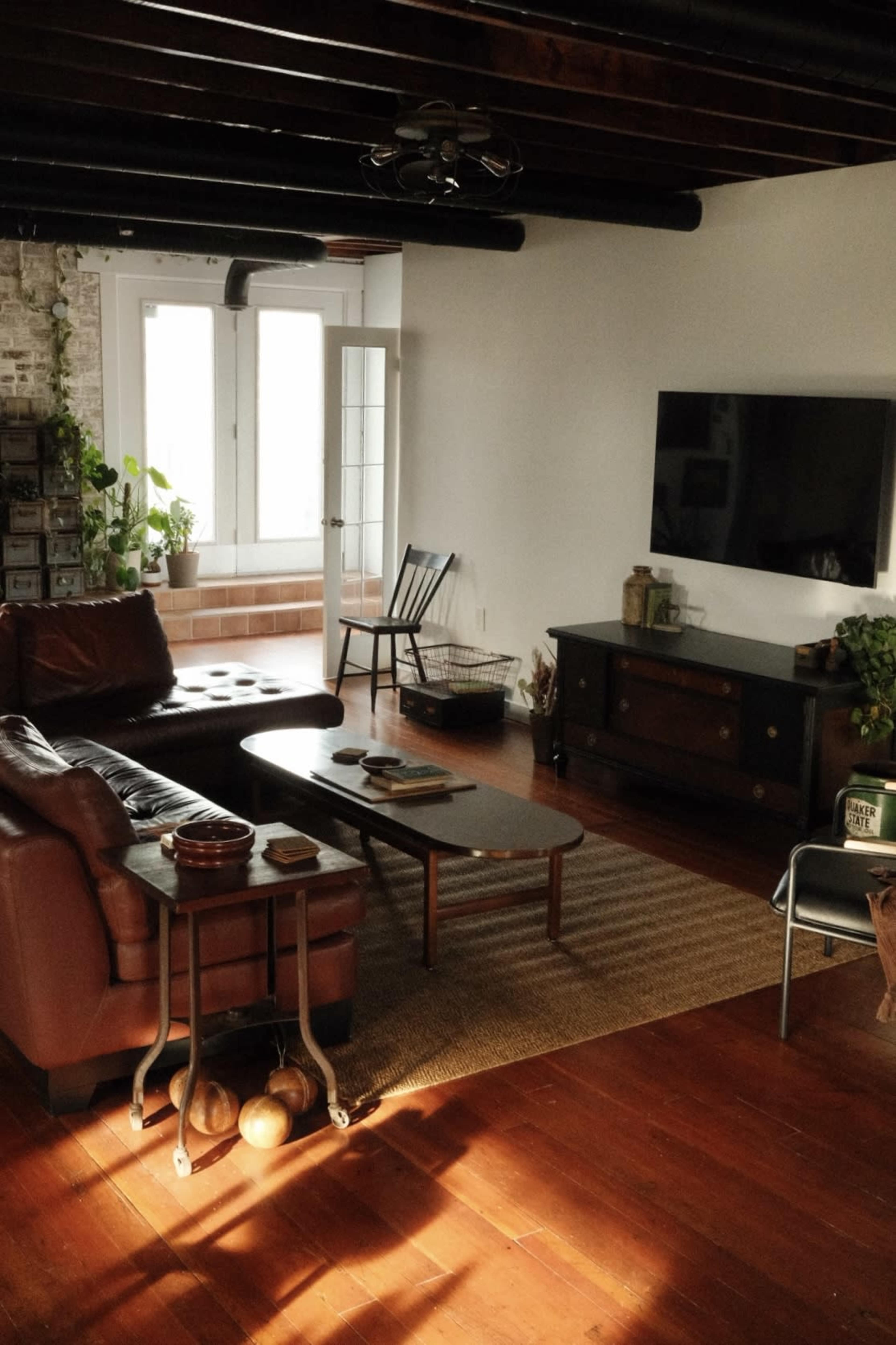 The living room features a leather sofa and a wooden coffee table, with a television mounted on a wall and large windows letting in natural light.