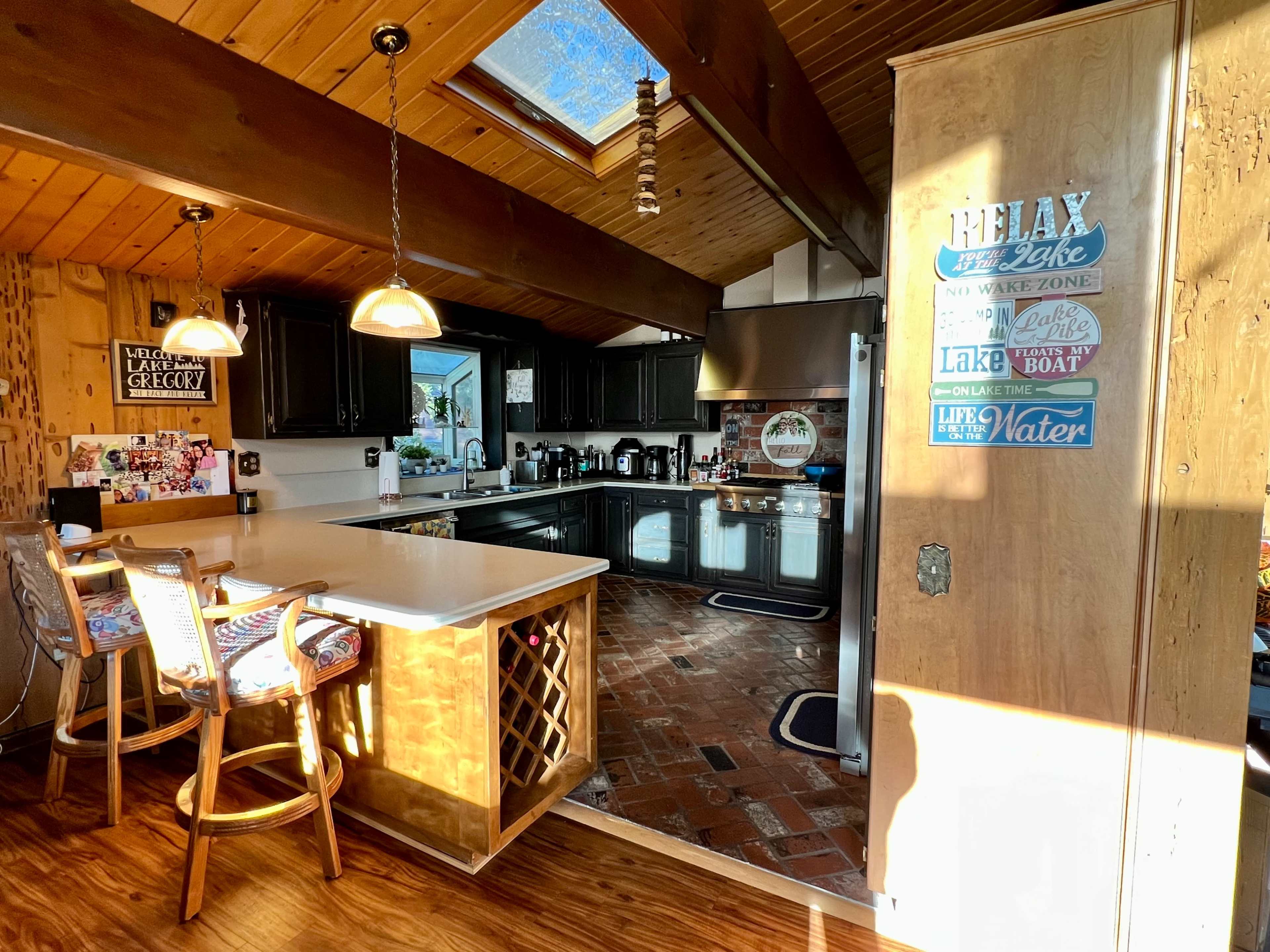 The kitchen features wooden beams, a skylight, and a mix of dark cabinetry and light countertops, with a wine rack and bar seating.
