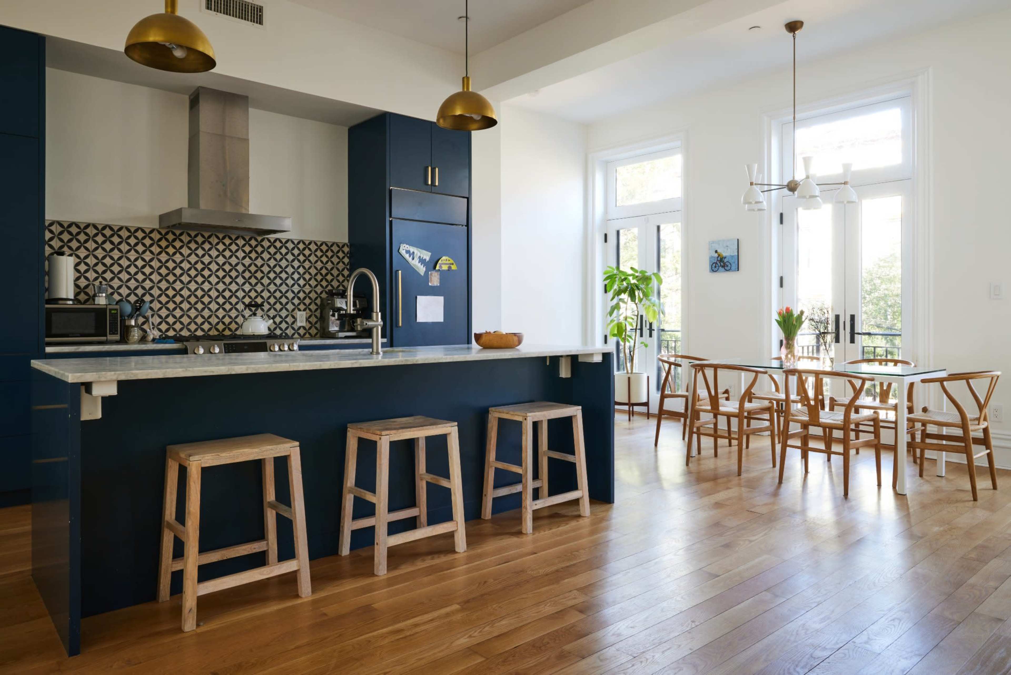 The image shows a modern kitchen with a blue cabinetry and a wooden dining area featuring a table and chairs.