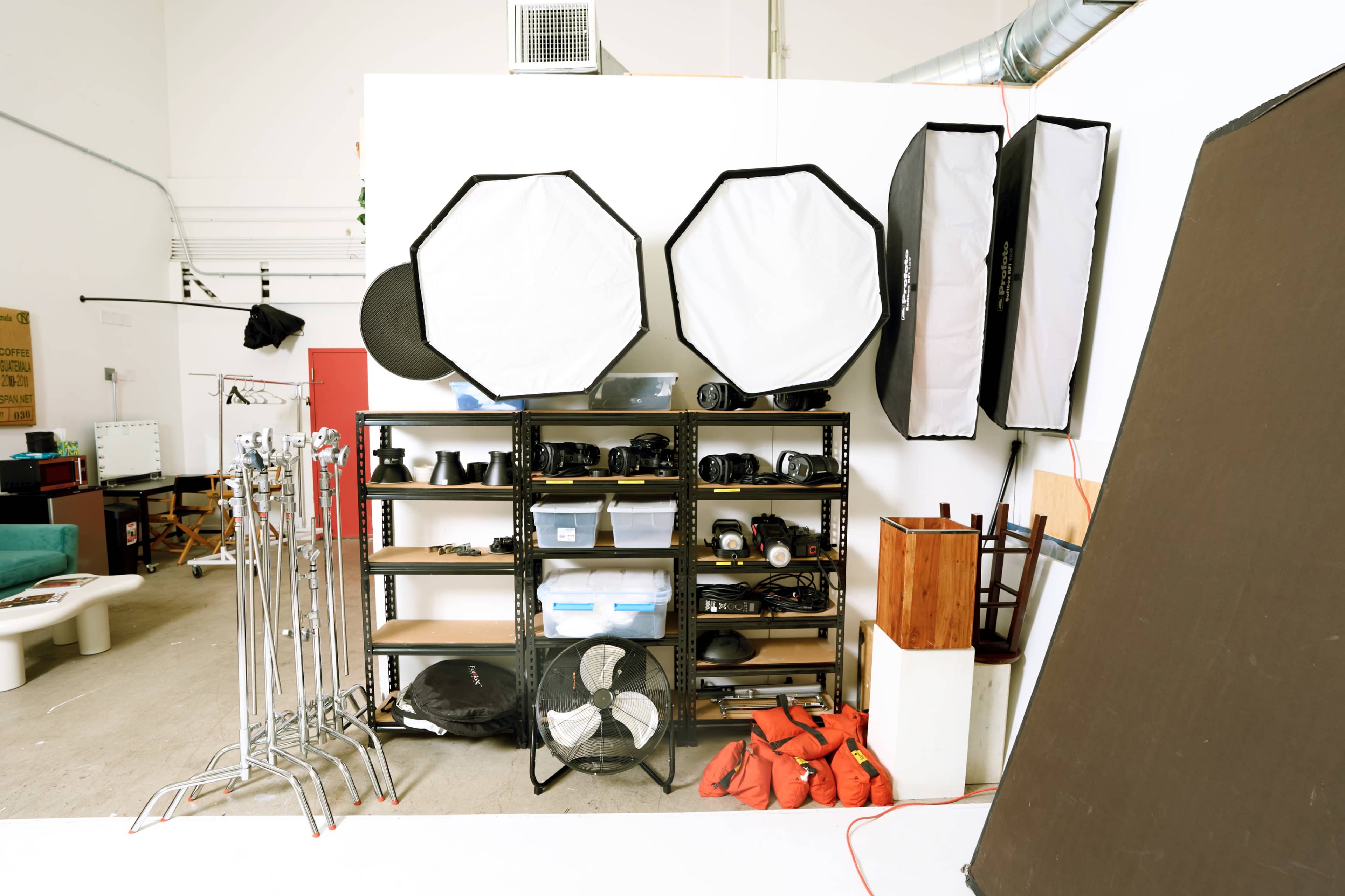 The image shows a photography studio setup with various lighting equipment, shelves filled with camera accessories, and a backdrop on the floor.