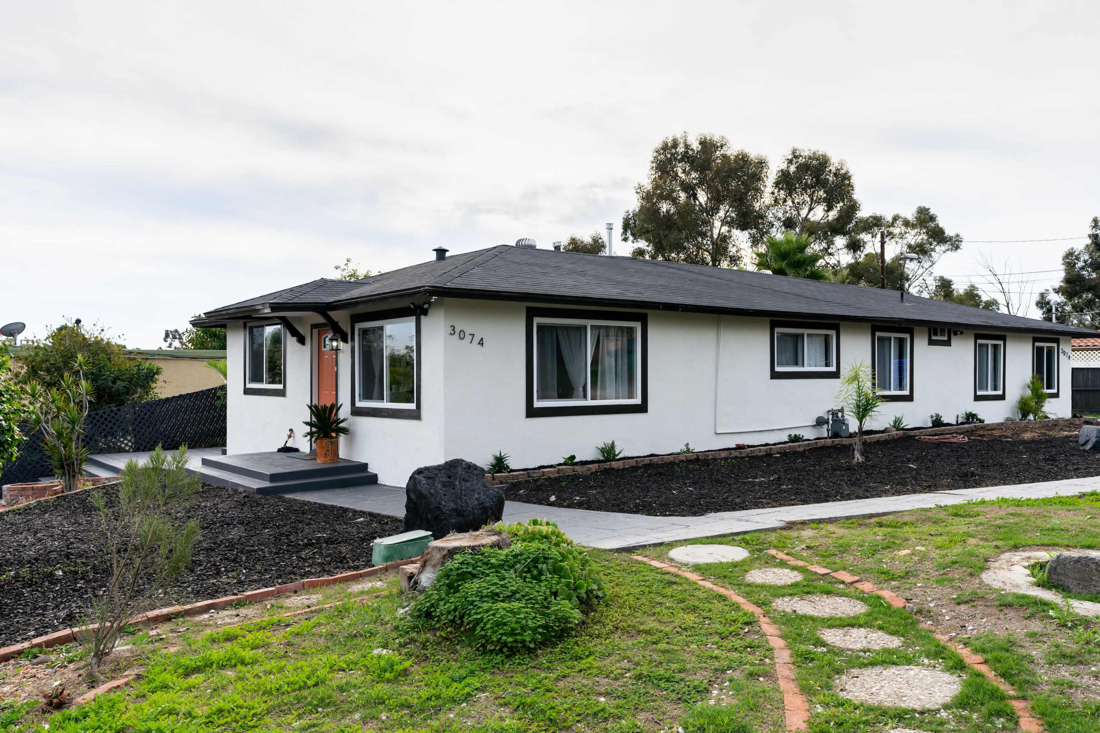 A single-story, modern white house with a black roof and landscaped yard is shown in the image.