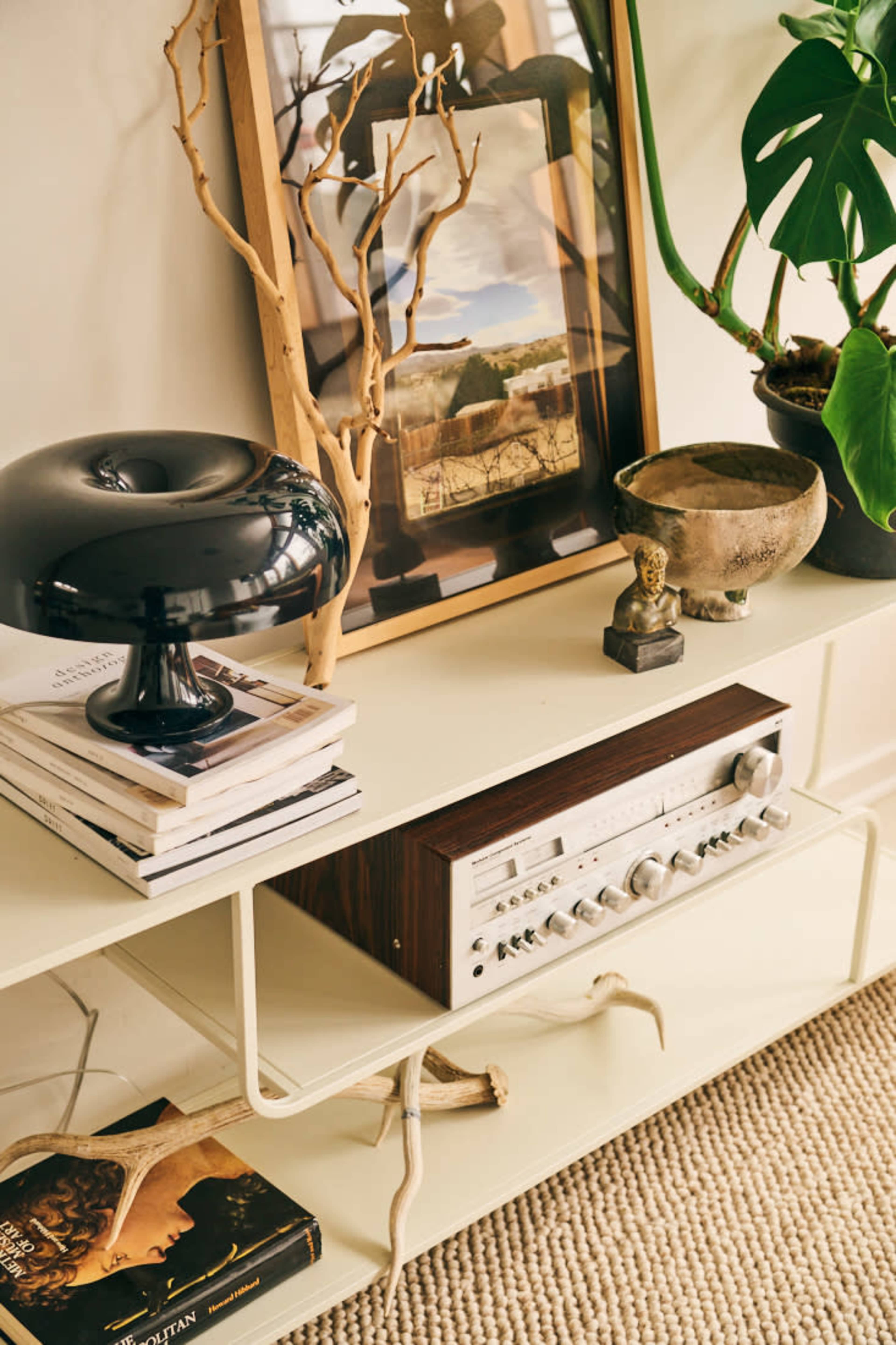 The image shows a stylish interior scene featuring a vintage audio receiver on a light-colored shelf, surrounded by books, a decorative bowl, a plant, and framed artwork.
