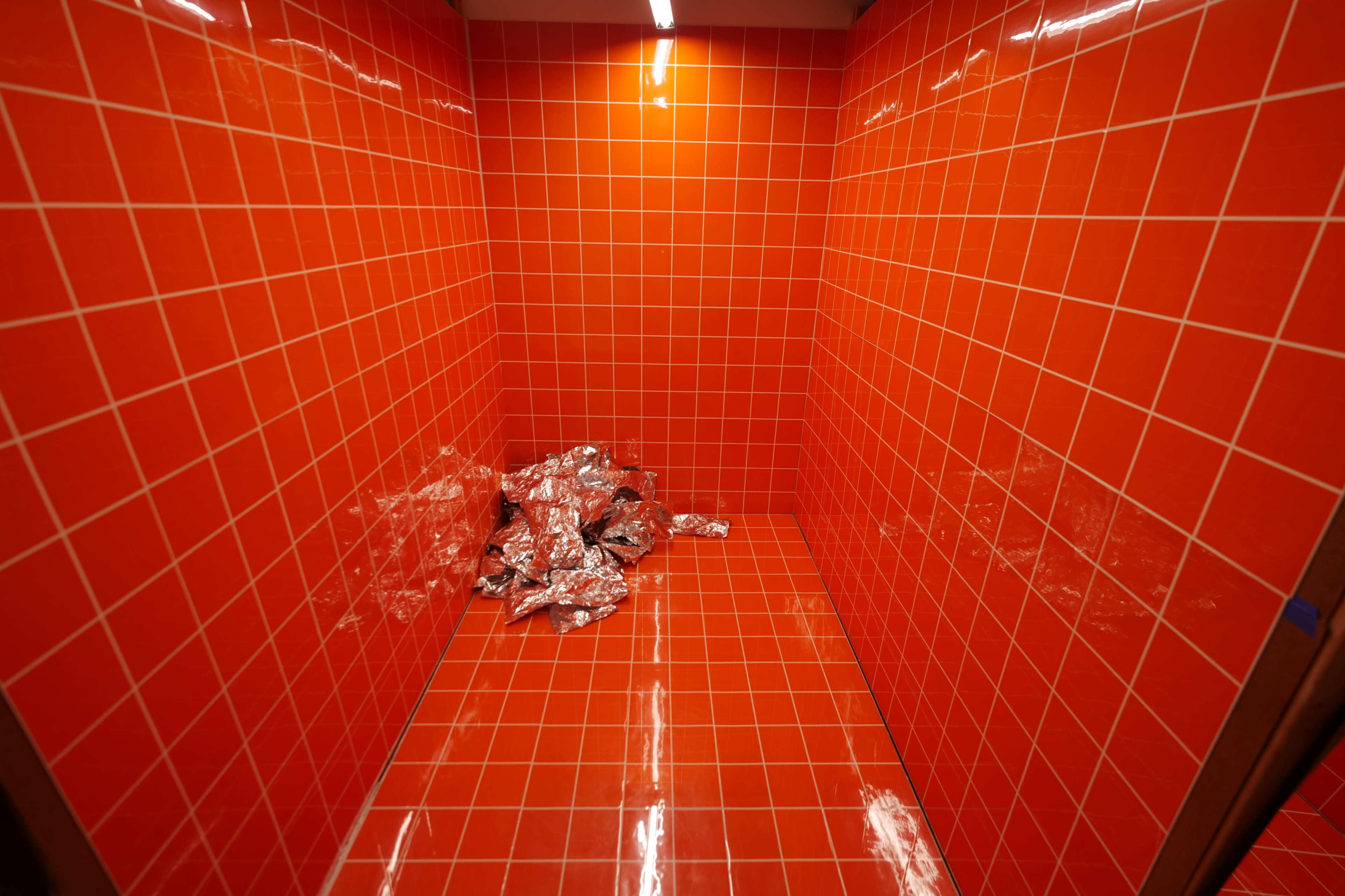 The image shows a small room with bright orange tiled walls and a shiny pile of crumpled aluminum foil in one corner.