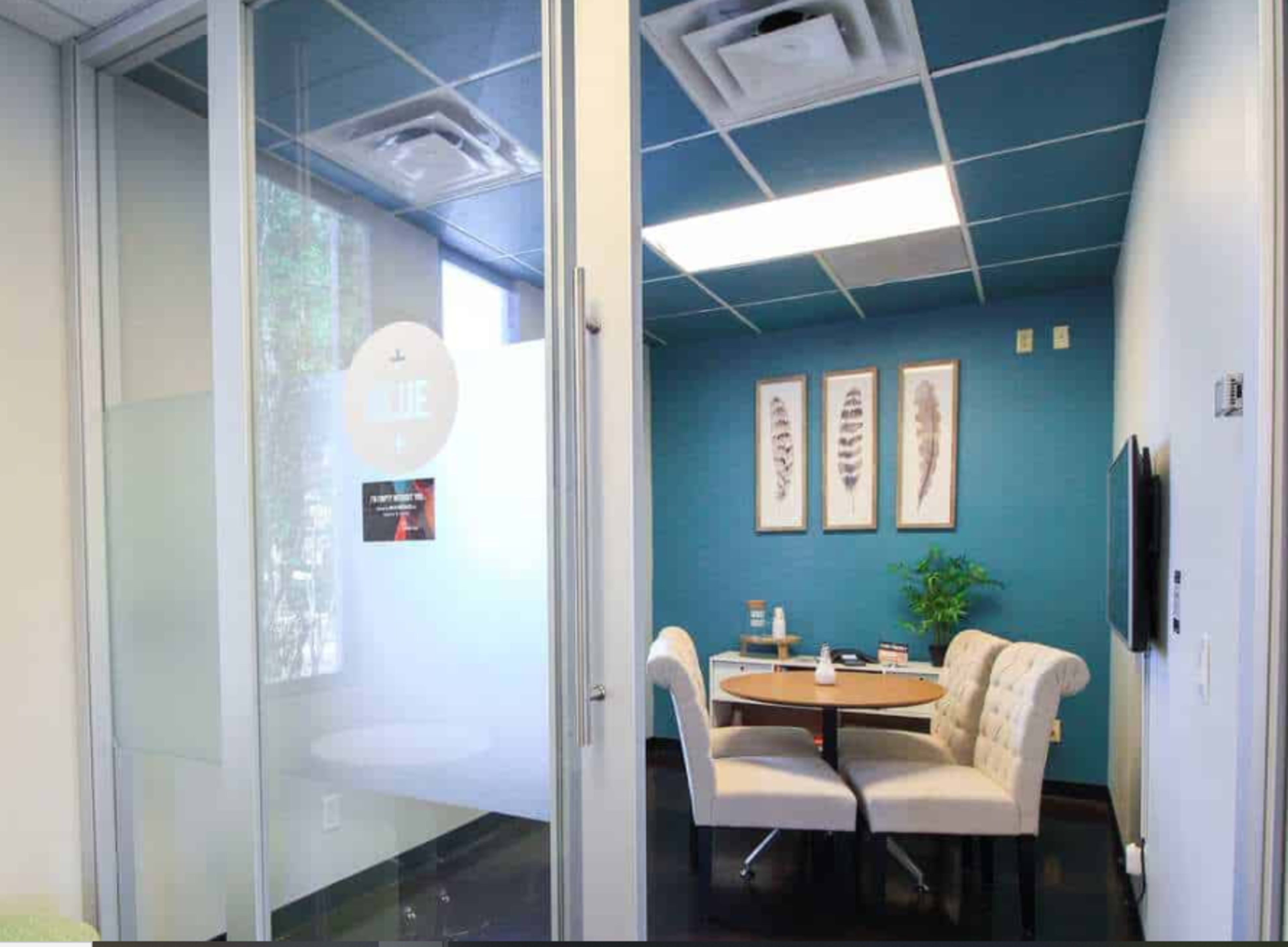 A small conference room features a round table with four upholstered chairs, surrounded by teal walls and framed artwork.