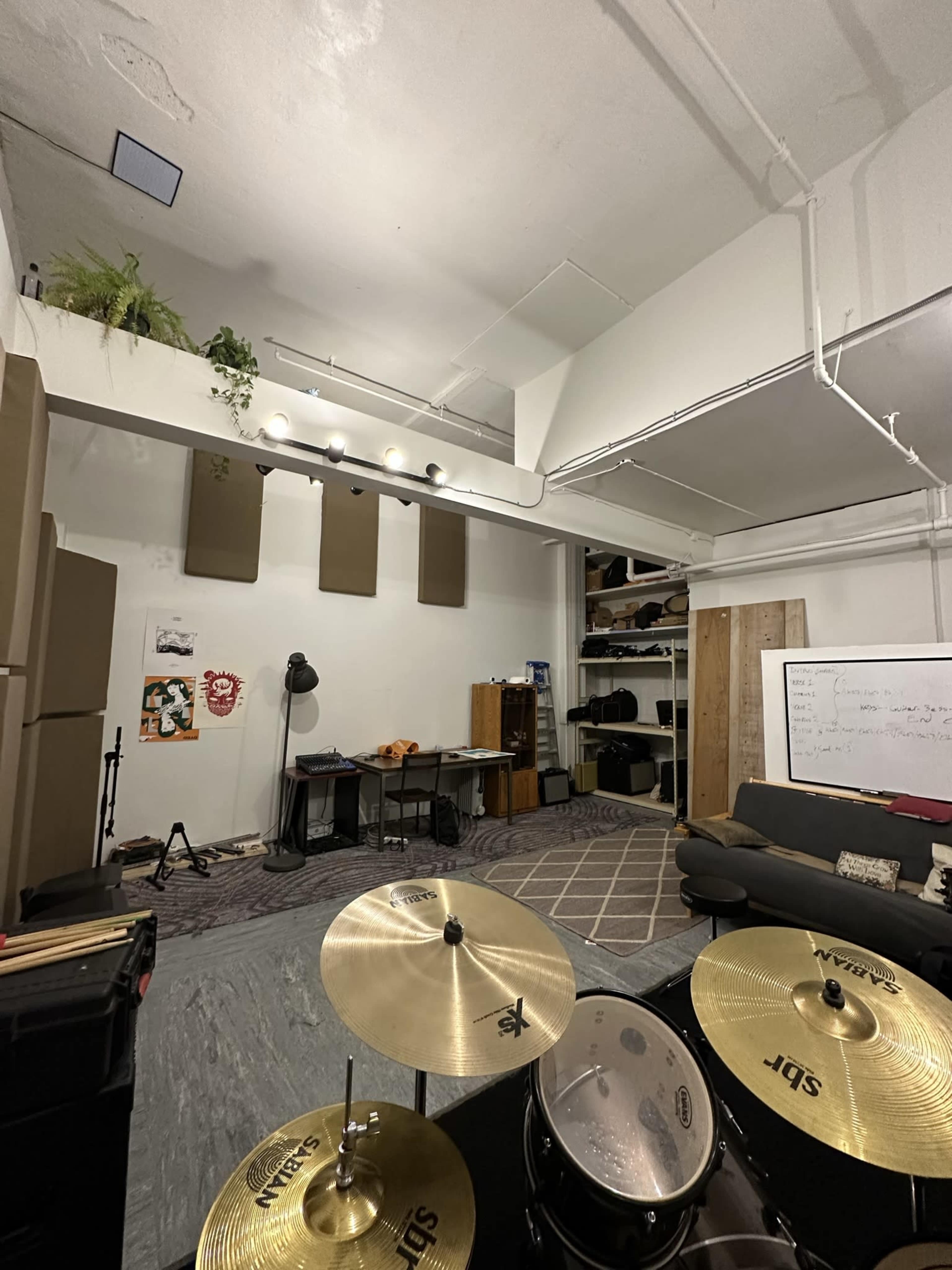 A music rehearsal space featuring a drum set, a couch, desks, and soundproofing on the walls.