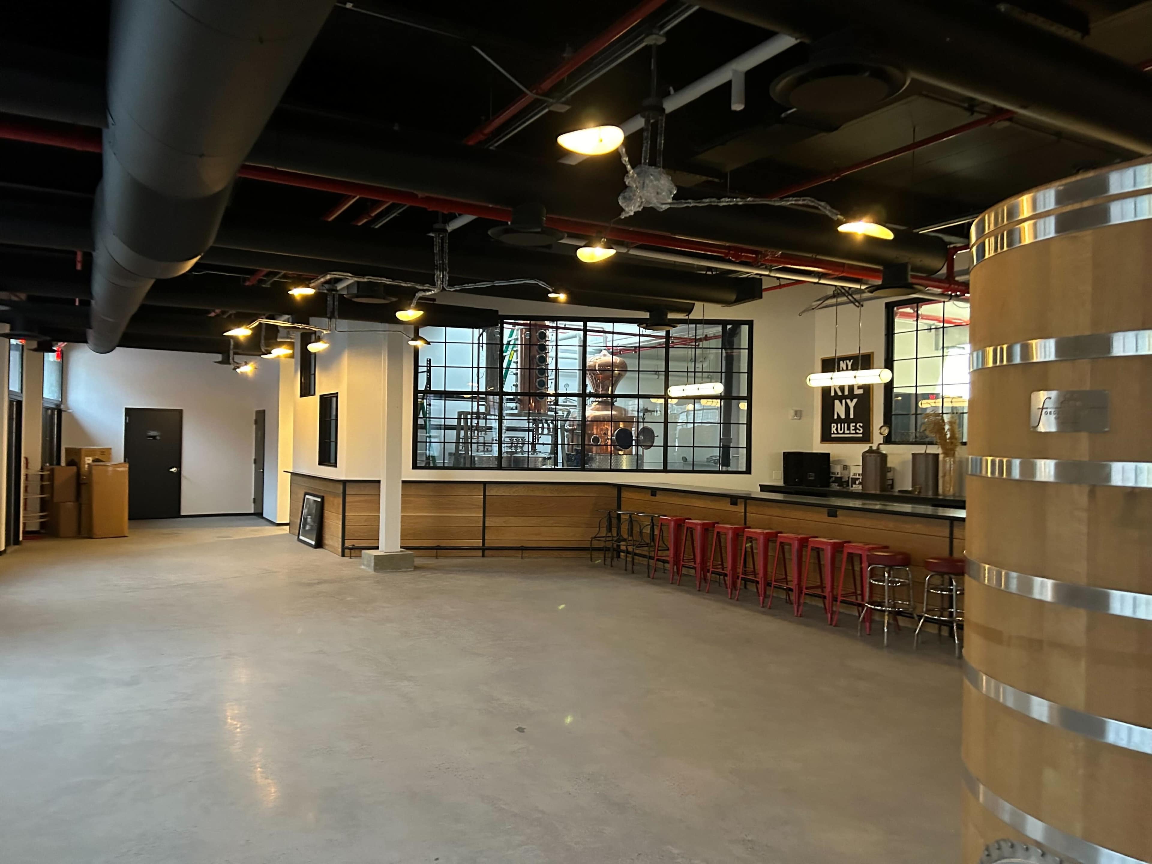 A spacious, industrial-style interior featuring a bar with red stools, large windows, and wooden paneling.