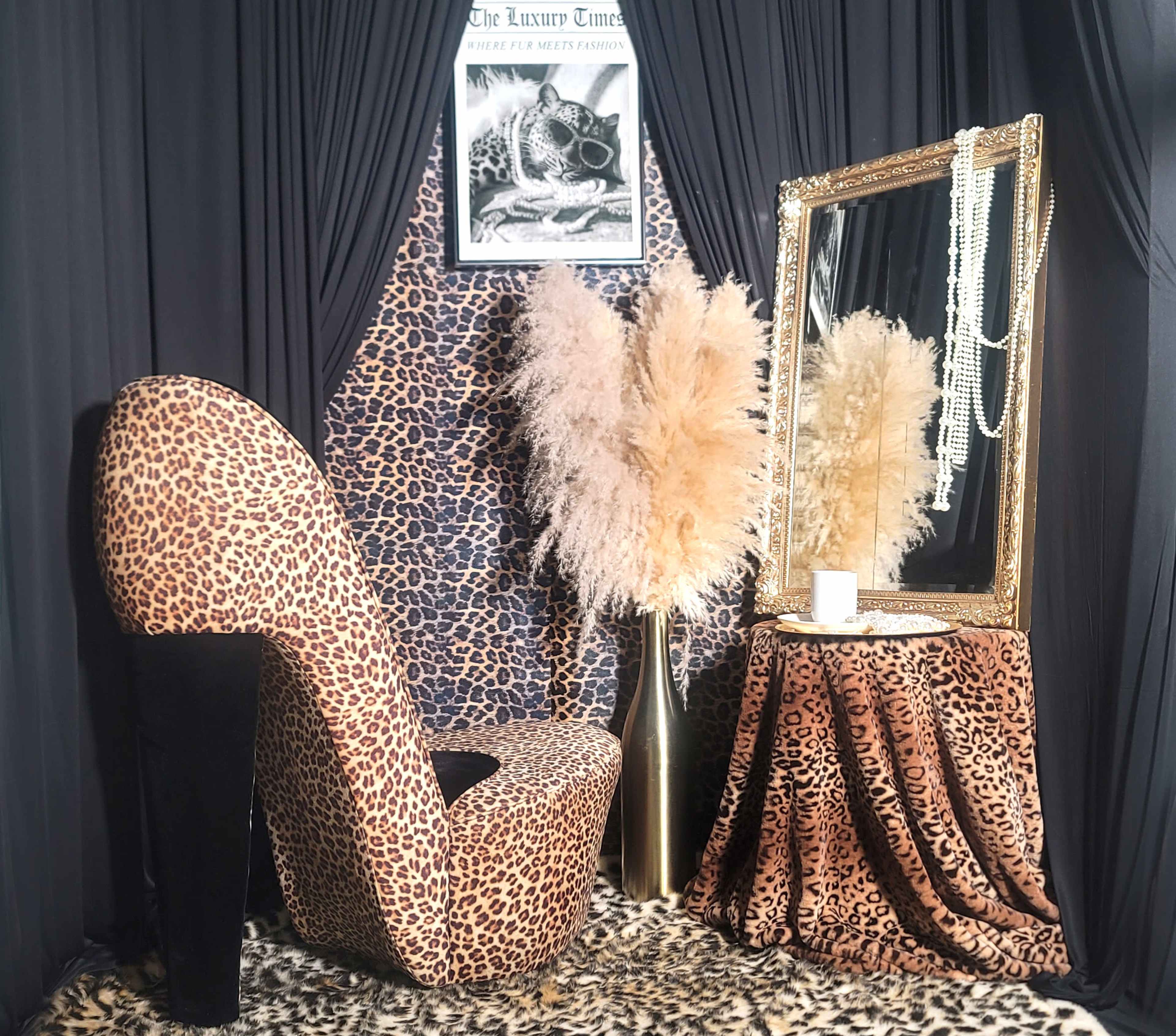 The scene features a stylish leopard-print lounge chair, a decorative mirror, and tall, feathery plants against a backdrop of leopard-patterned fabric.