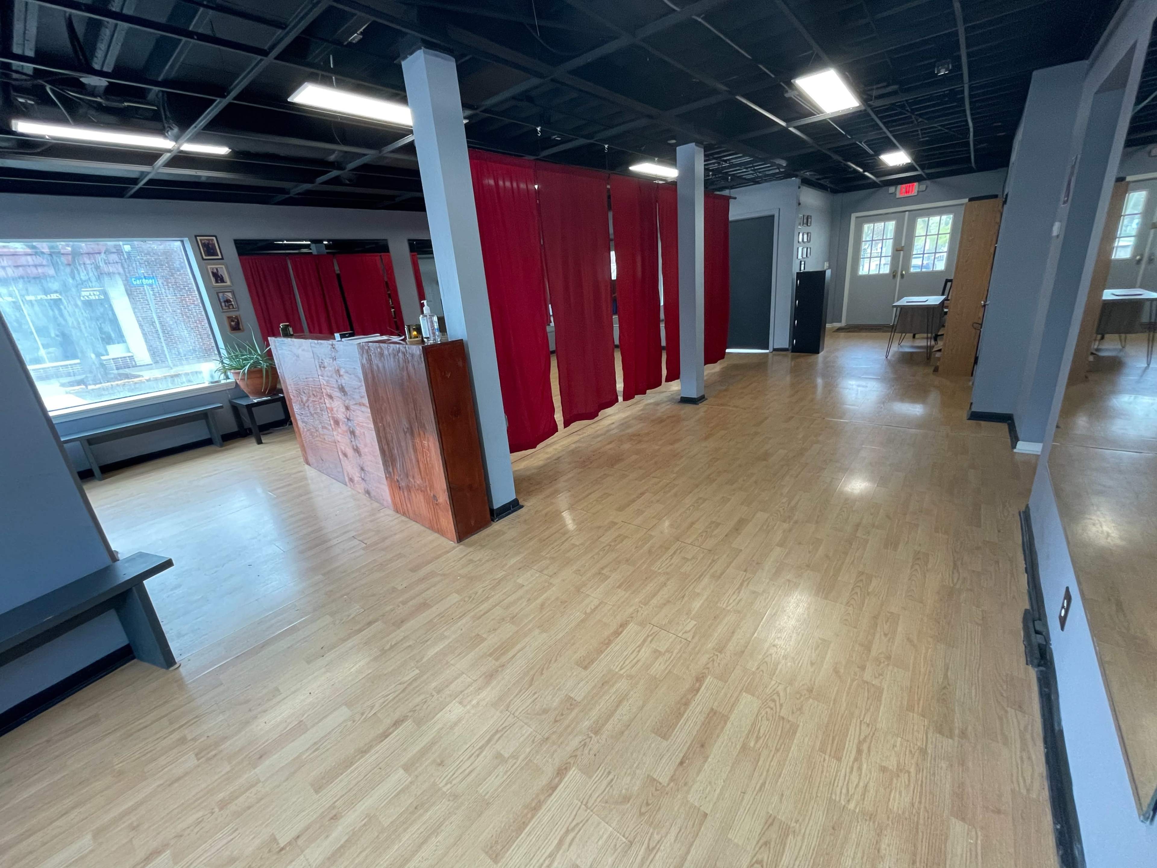 An empty interior space with a wooden bar, red curtains, and wooden flooring.