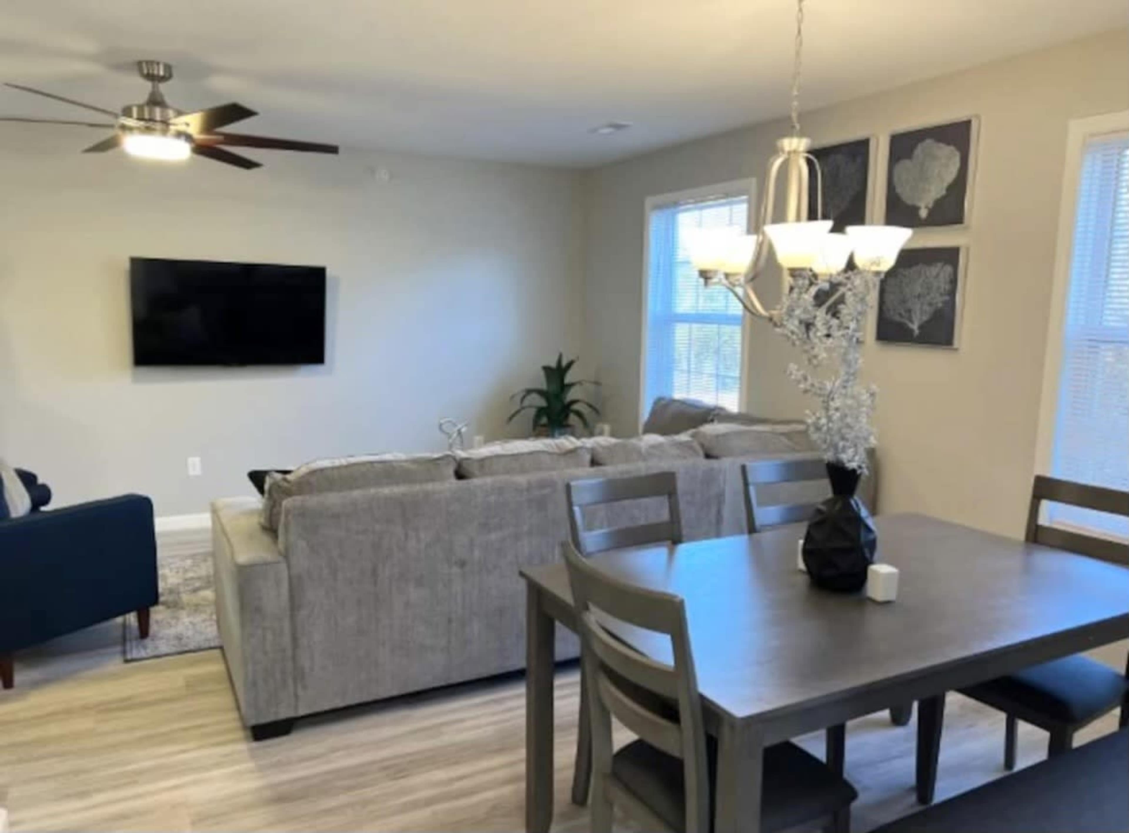 A living and dining area with a gray sectional sofa, a wooden dining table with chairs, and a wall-mounted television.