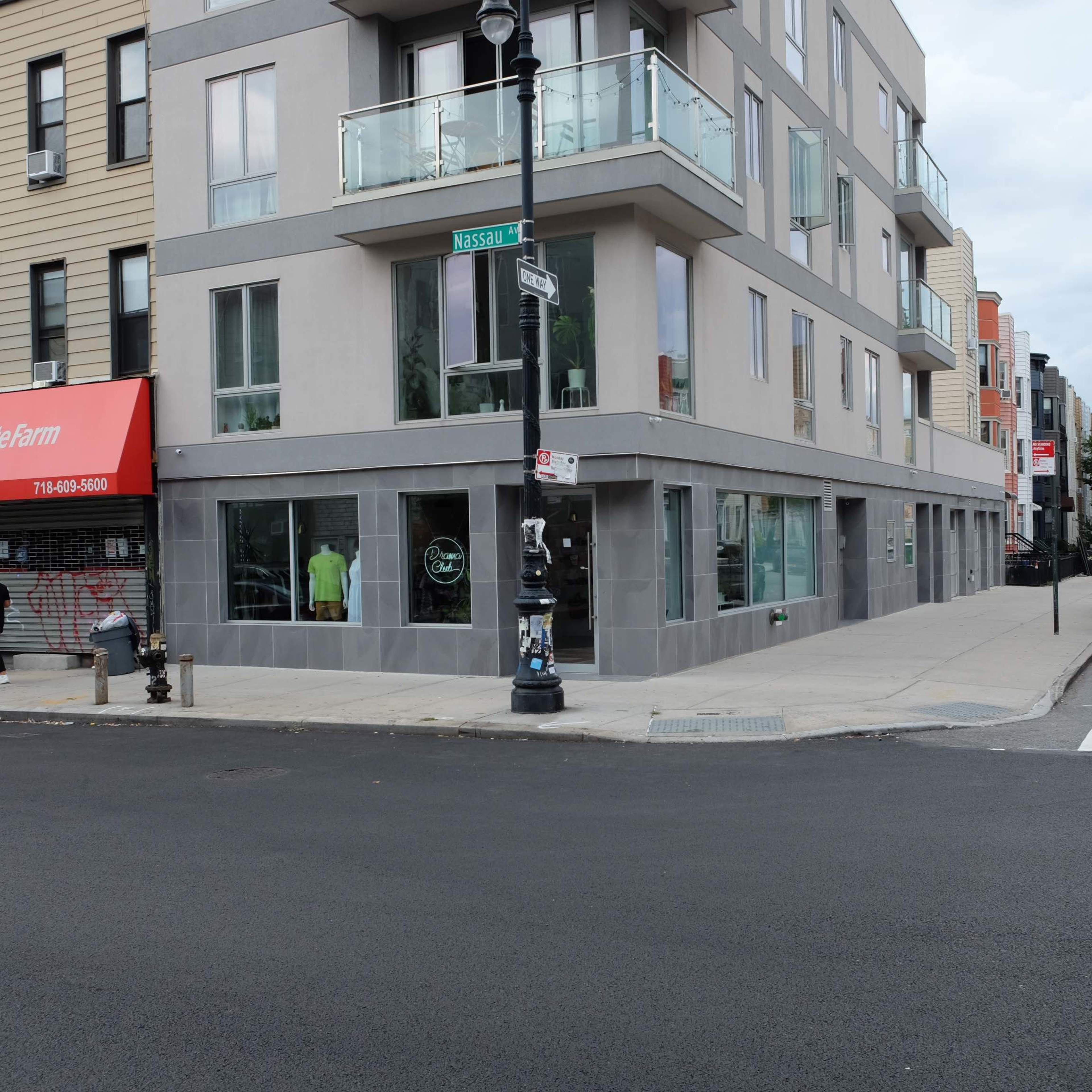 A modern building with large windows and balconies sits at the corner of Nassau Street and a side street, adjacent to a storefront with a red awning.