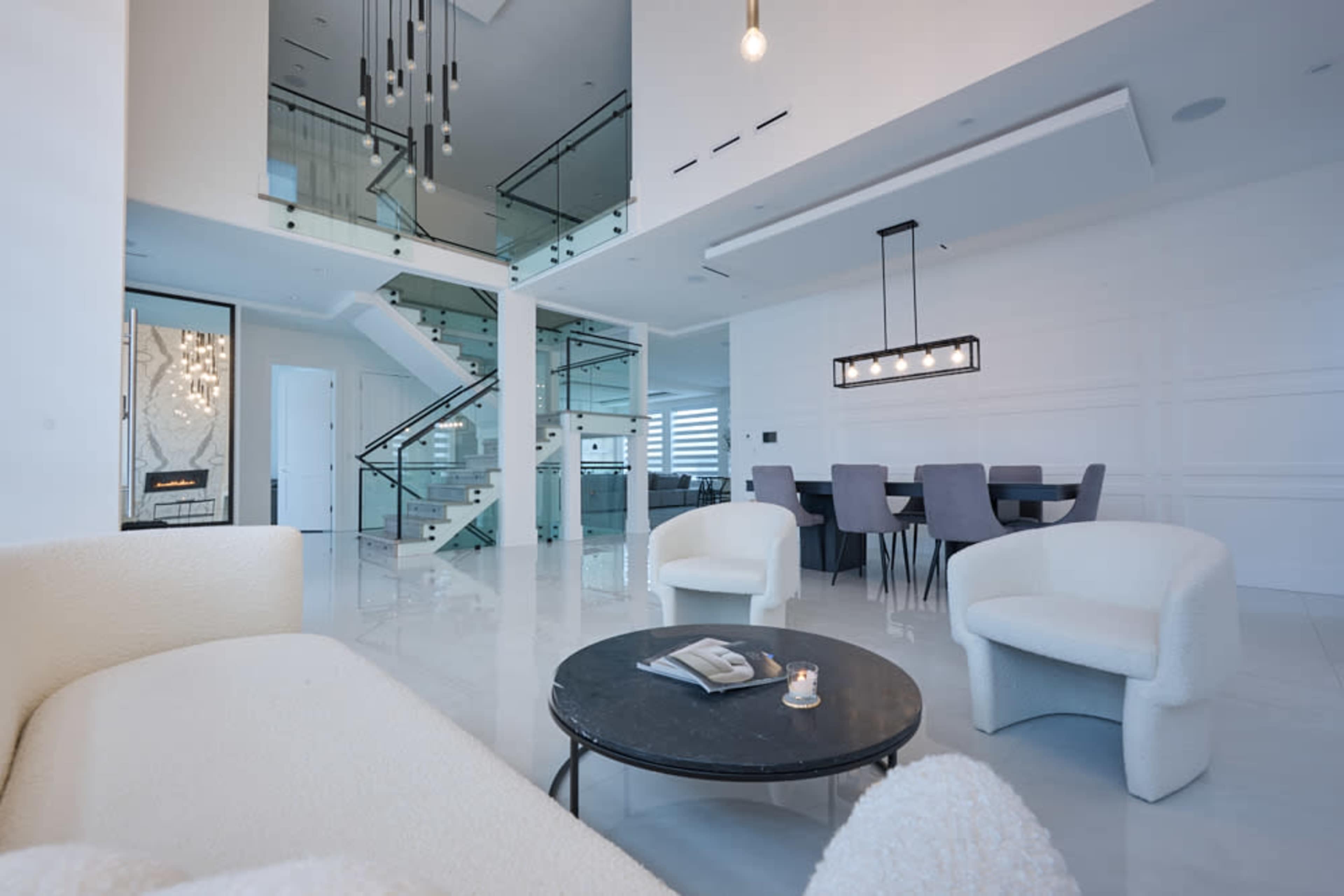 A modern, open-concept living space featuring a staircase, a dining area with gray chairs, and contemporary furniture.