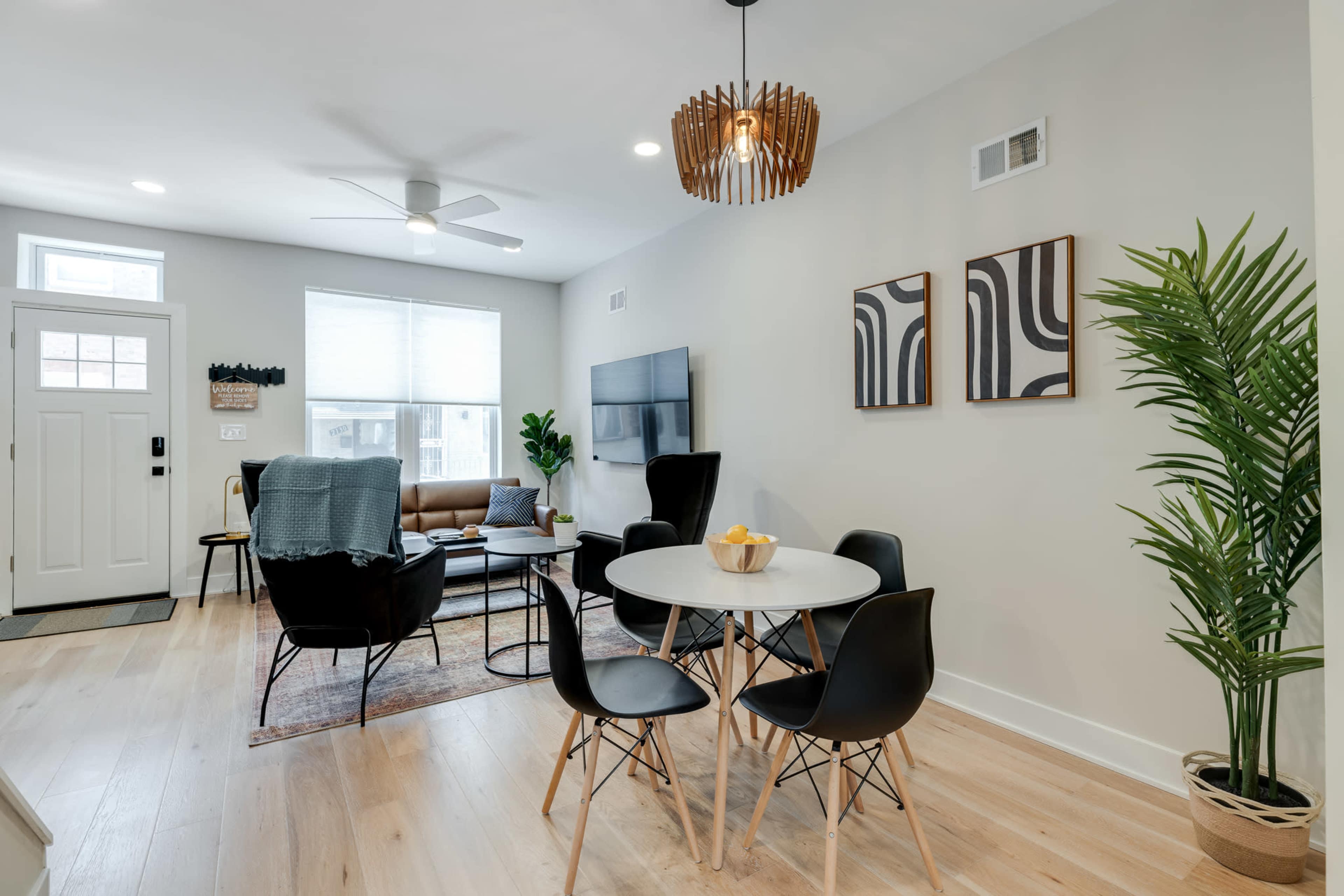A modern living space featuring a dining area with a circular table and black chairs, a seating area with a brown couch, and a wall-mounted television.