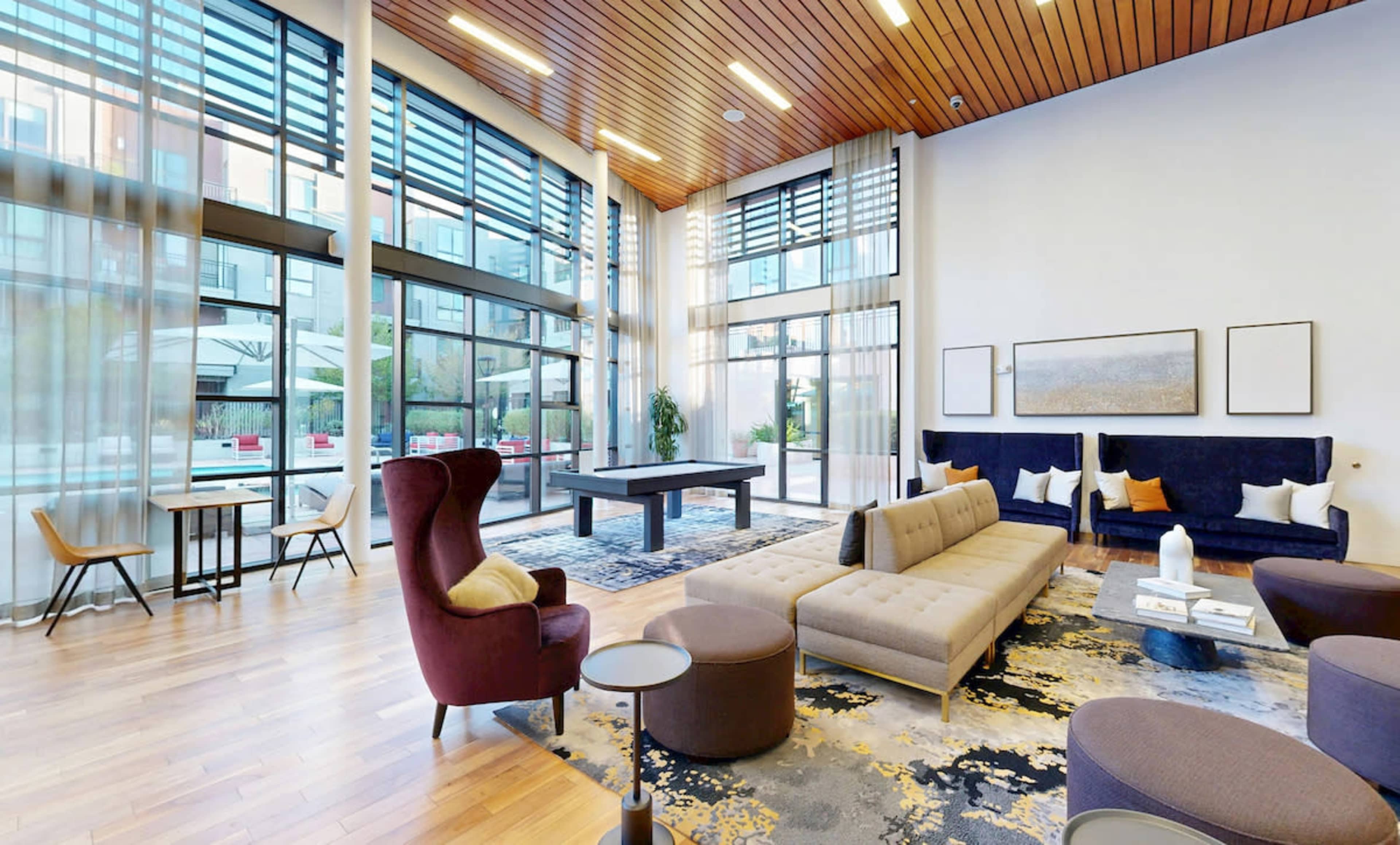 The image shows a spacious, modern lounge area with large windows, comfortable seating arrangements, and a pool table.