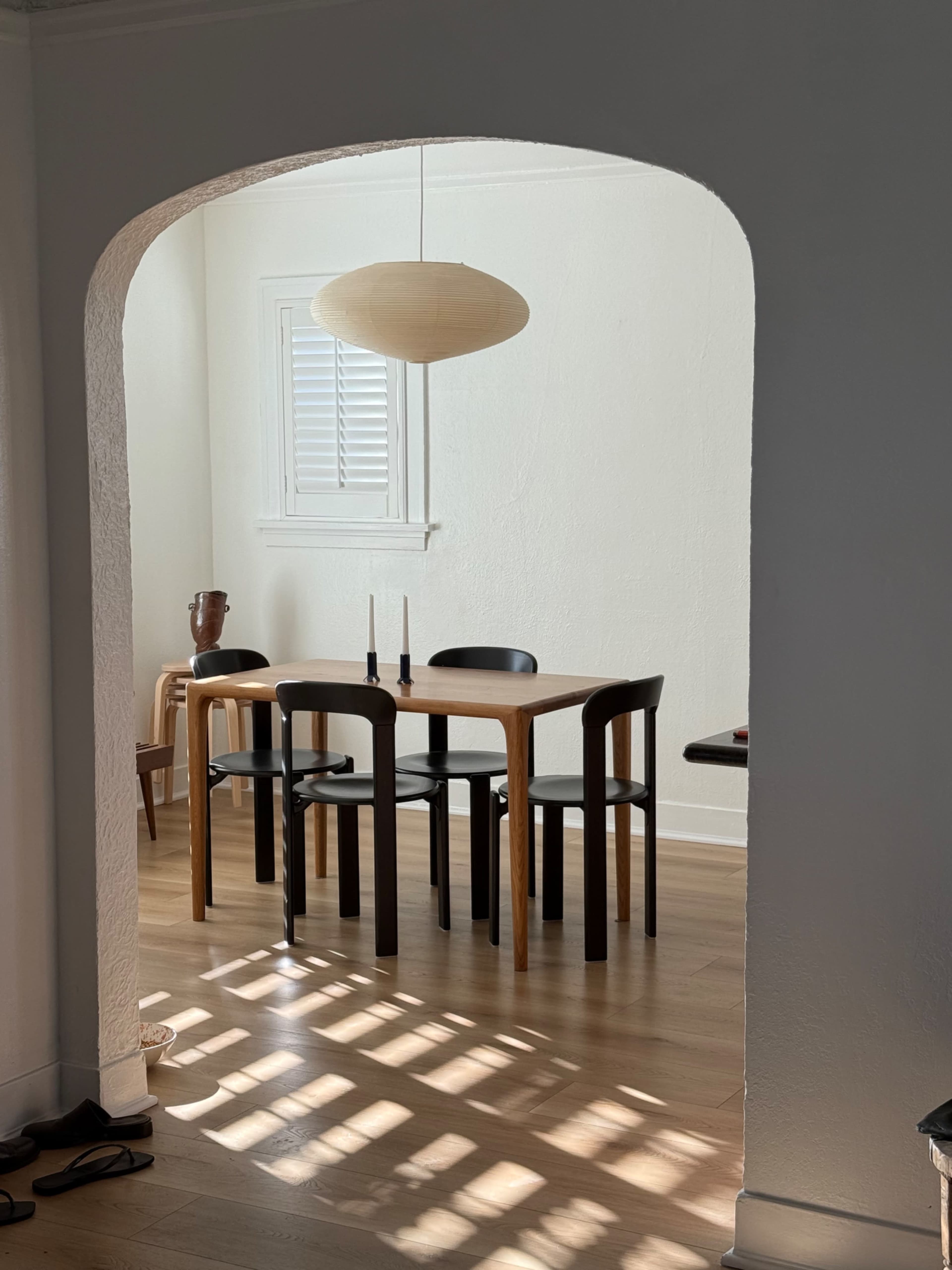 A dining area features a wooden table with four chairs, illuminated by natural light streaming through a nearby window.