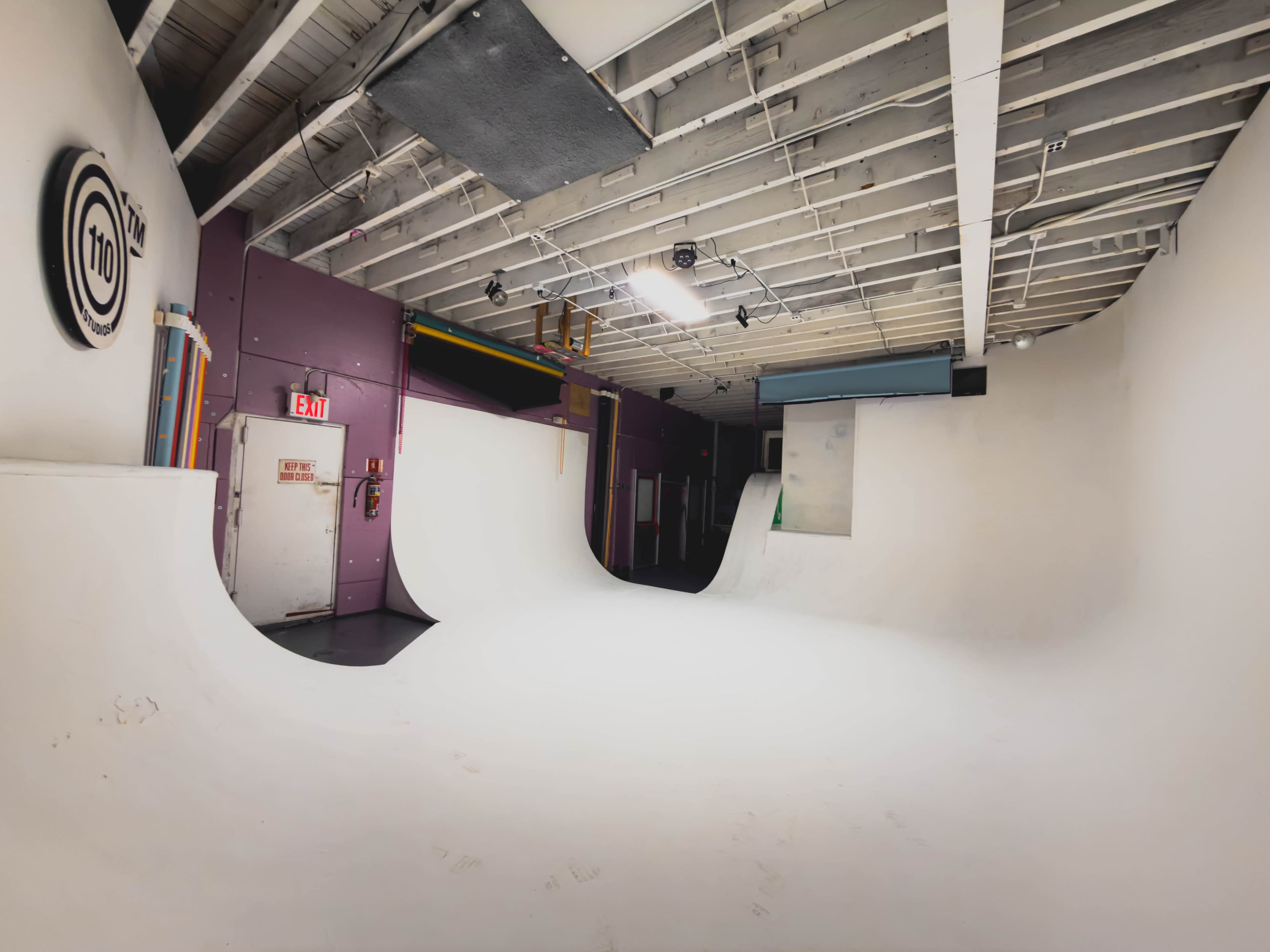 The image shows an empty indoor skate park with smooth white curved ramps and muted walls.