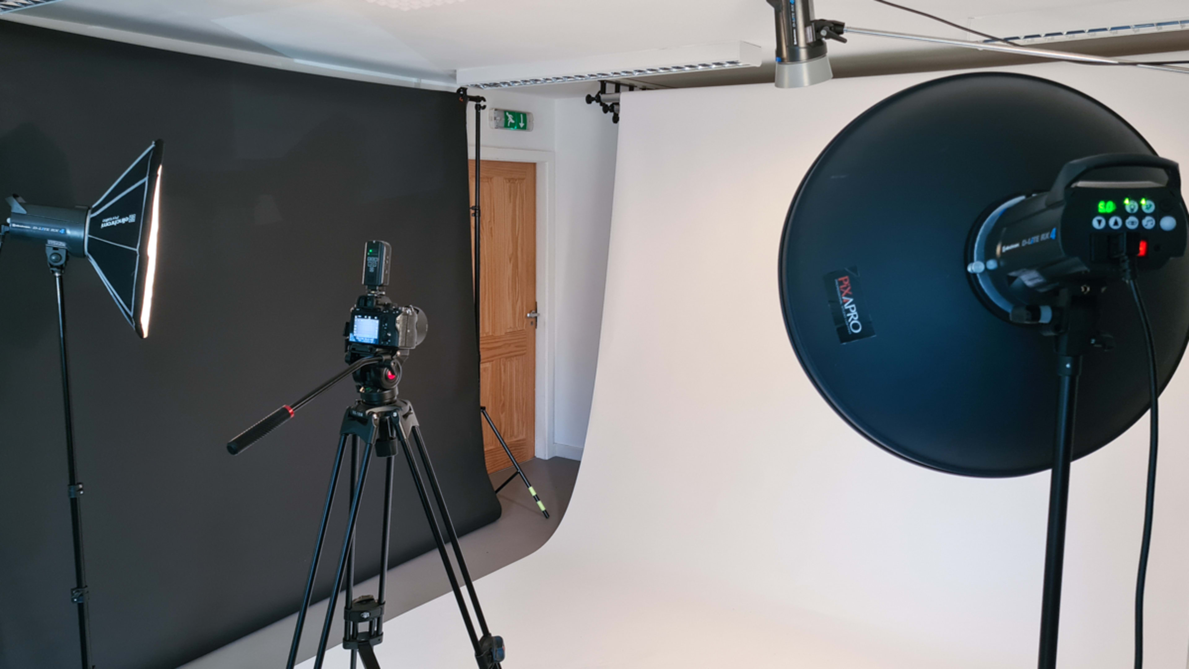 A photography studio setup with a camera on a tripod, two light sources, and two backdrops in black and white.