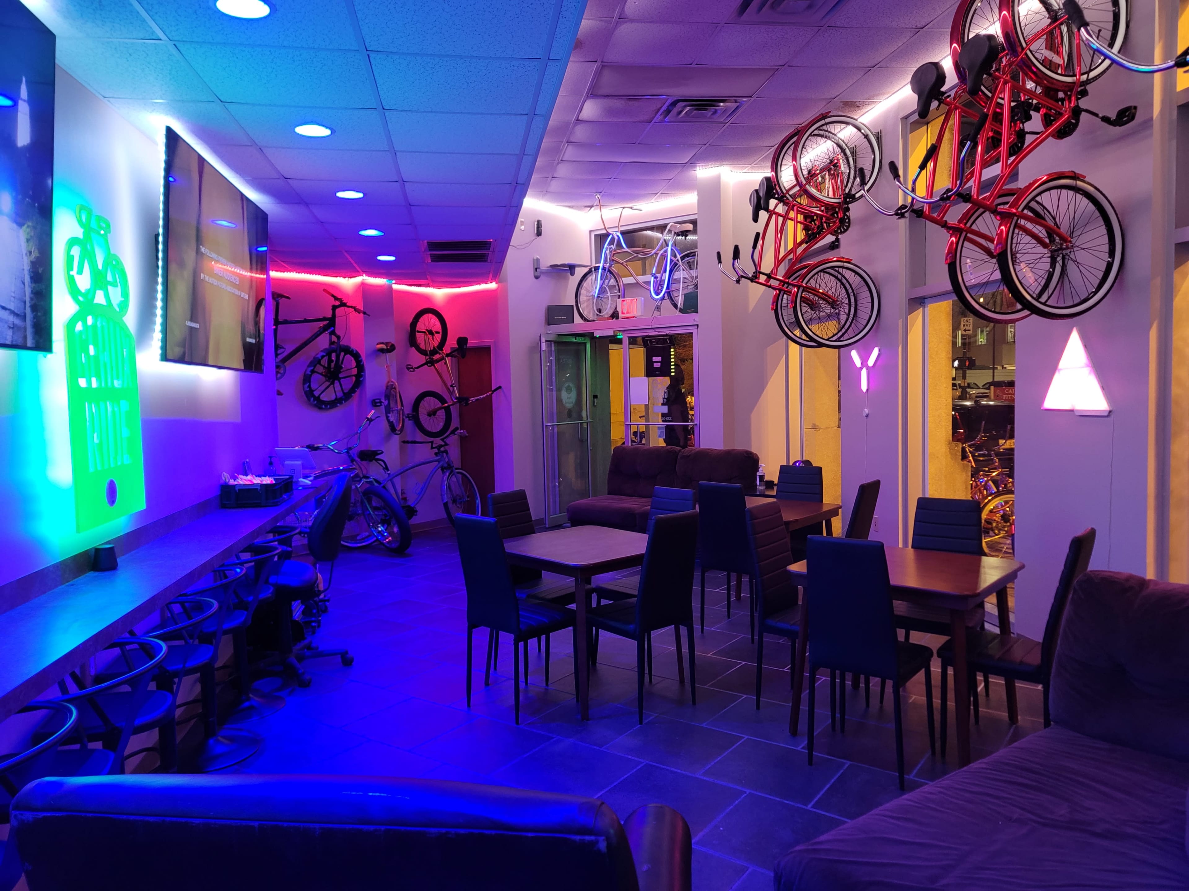 A lounge area with several tables and chairs, illuminated by colored lights and decorated with bicycles mounted on the walls.
