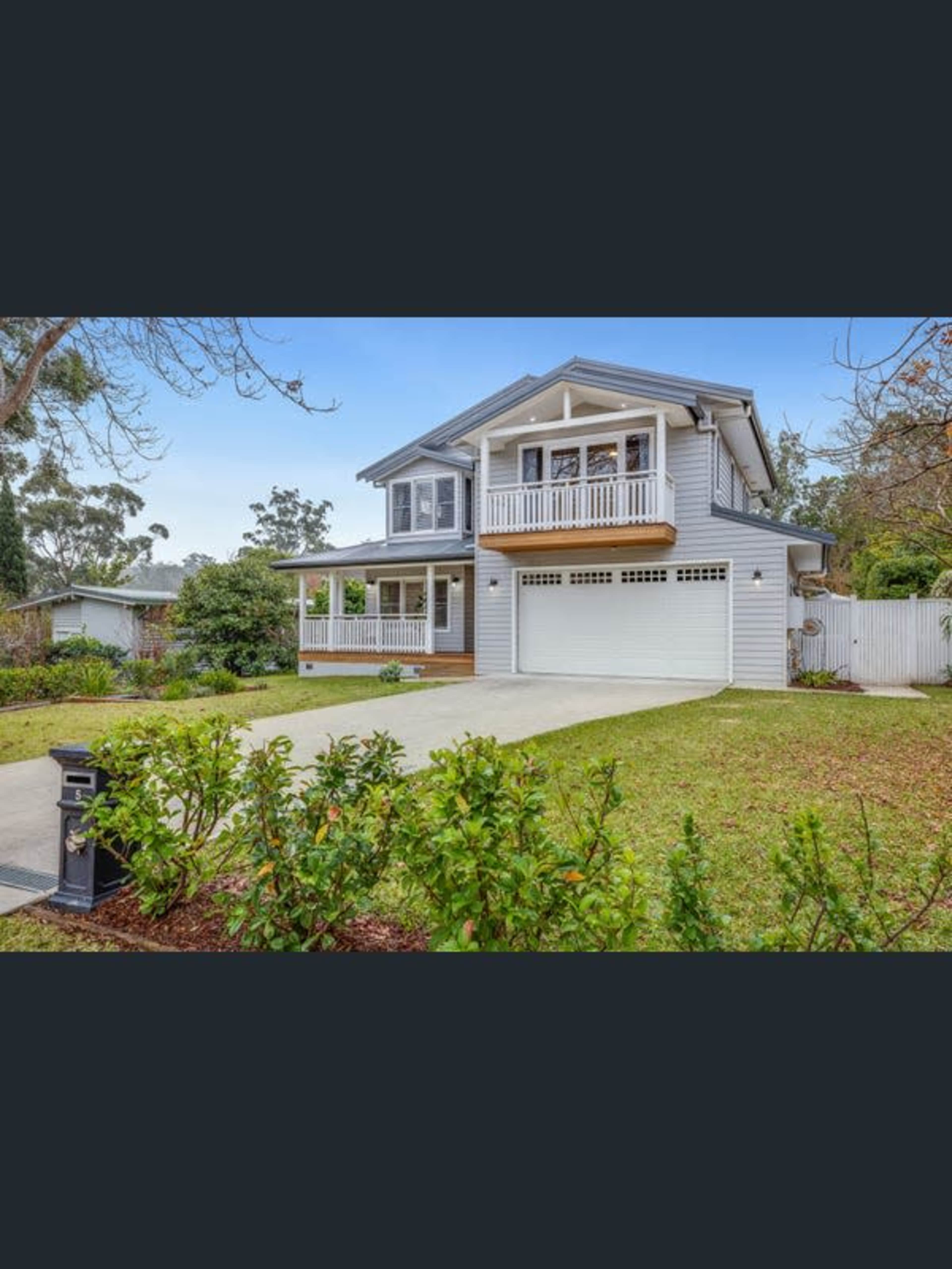 A two-story, light-colored house with a front porch and a garage sits in a landscaped yard.