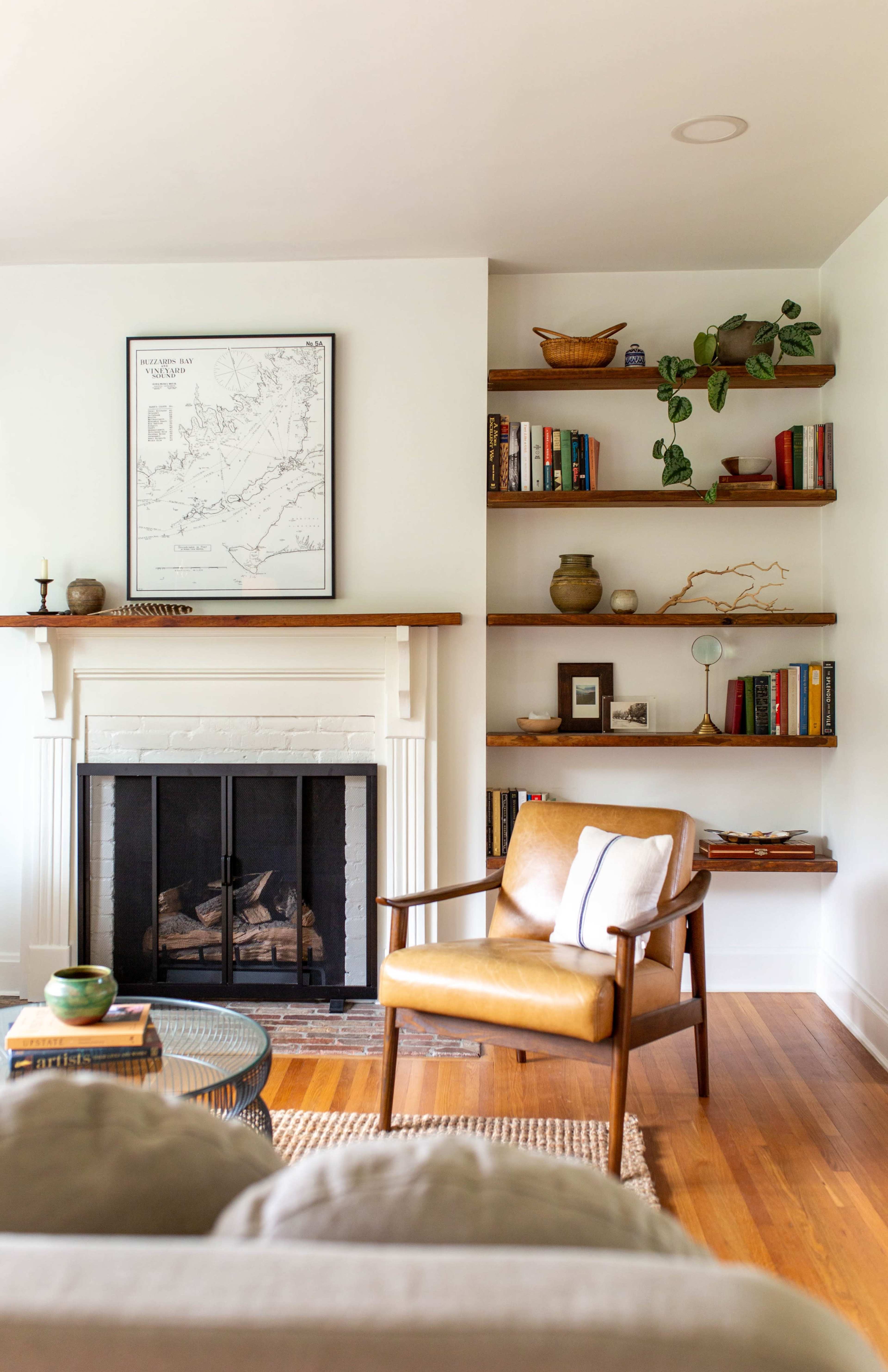 A living room with a fireplace, wooden shelves filled with books and decor, and a brown leather chair facing the fireplace.