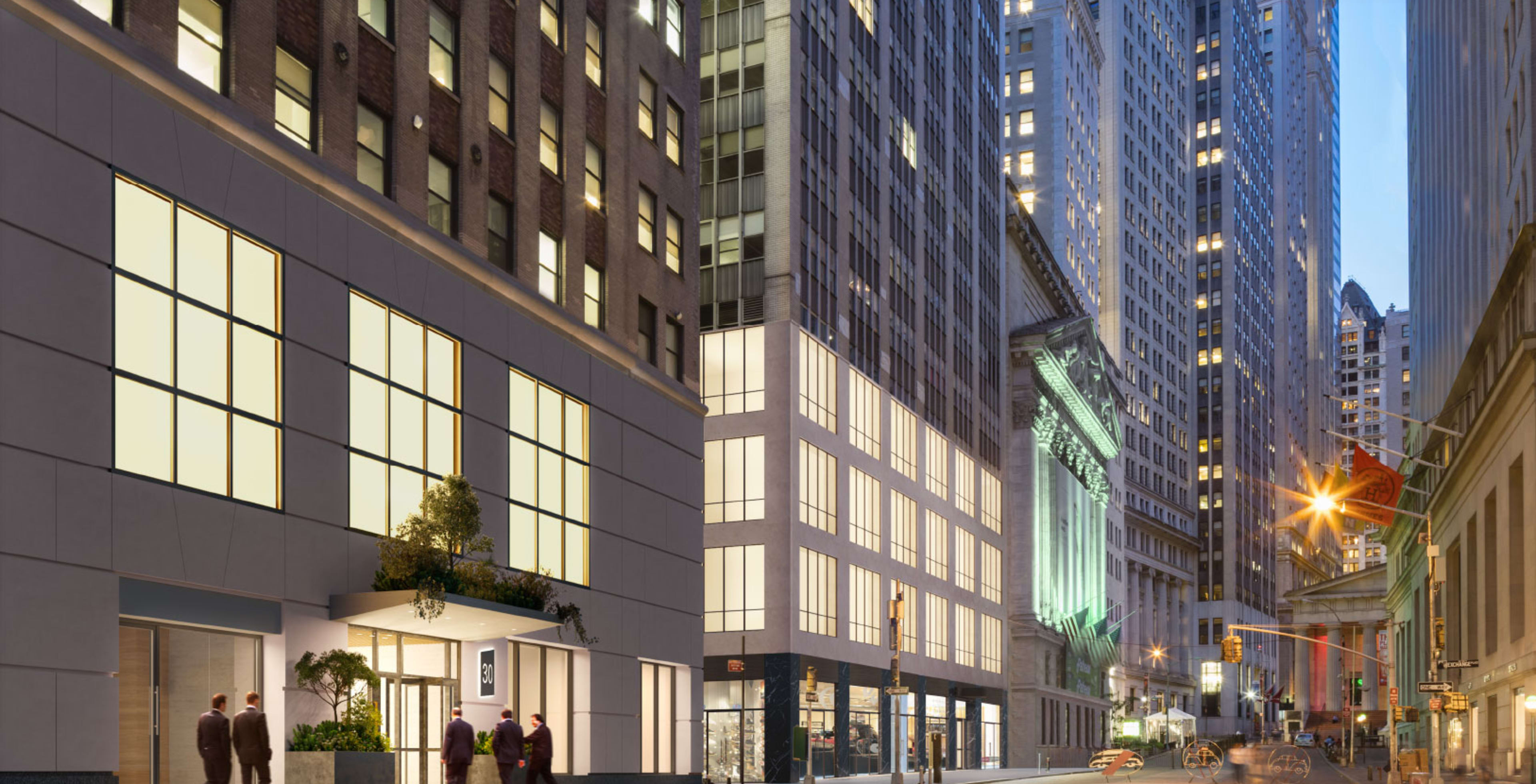 The image shows a city street scene featuring tall buildings, with a modern structure on the left and illuminated windows along the sidewalk.