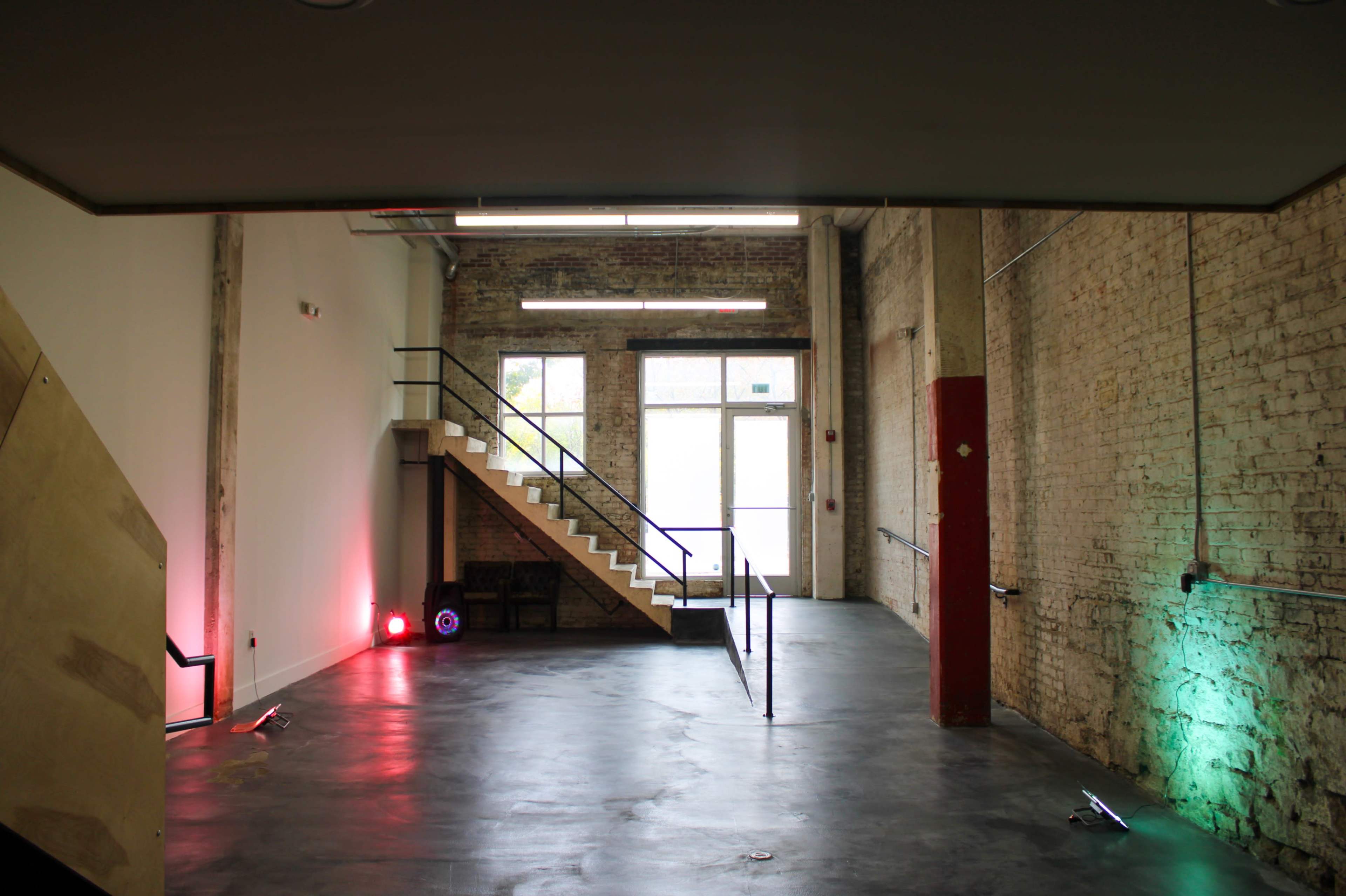 The image shows an interior space with a staircase on the left, large windows at the front, and a polished concrete floor.