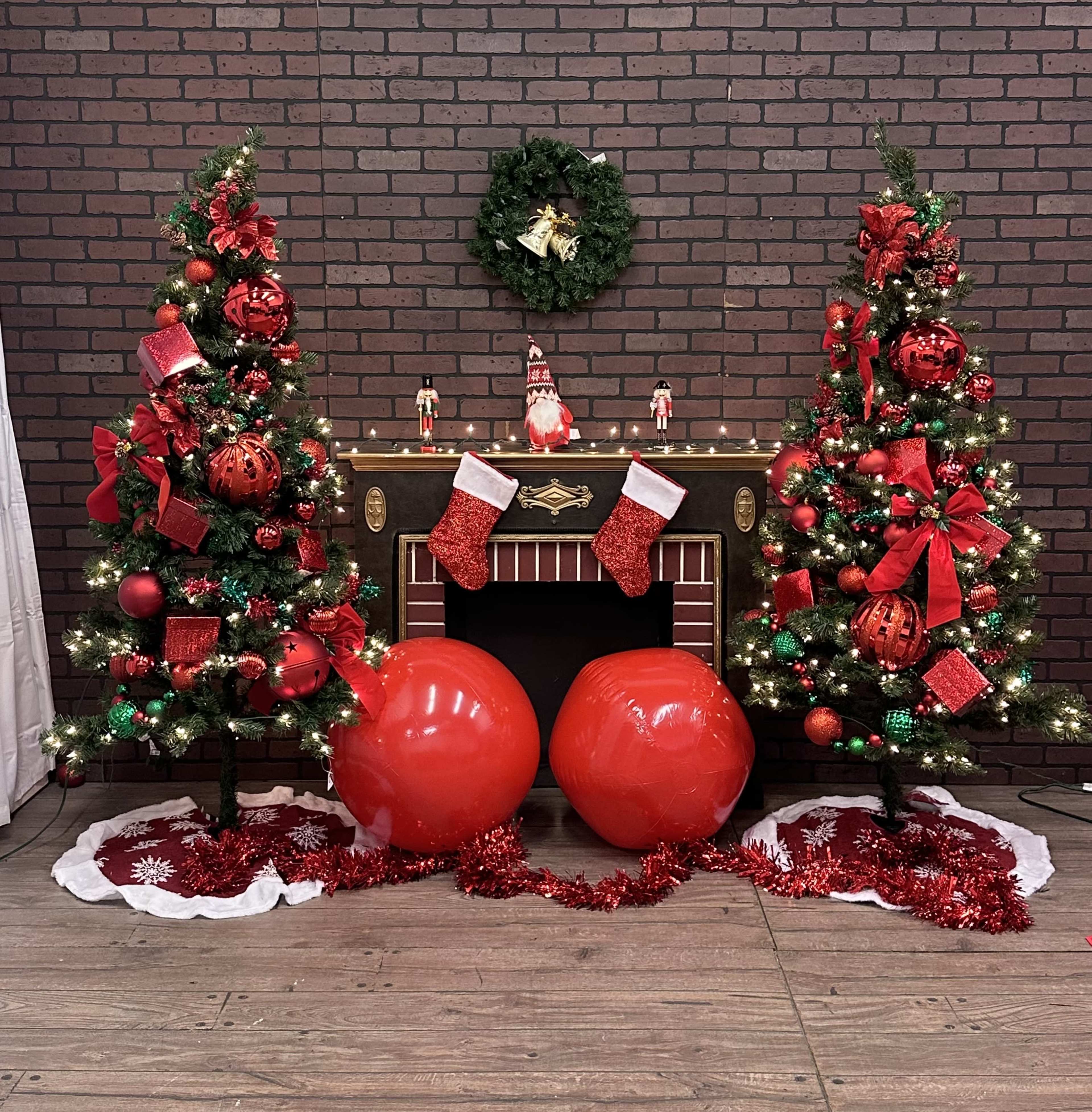 The scene features two decorated Christmas trees on either side of a fireplace, adorned with red ornaments and lights, surrounded by red and white decorations.