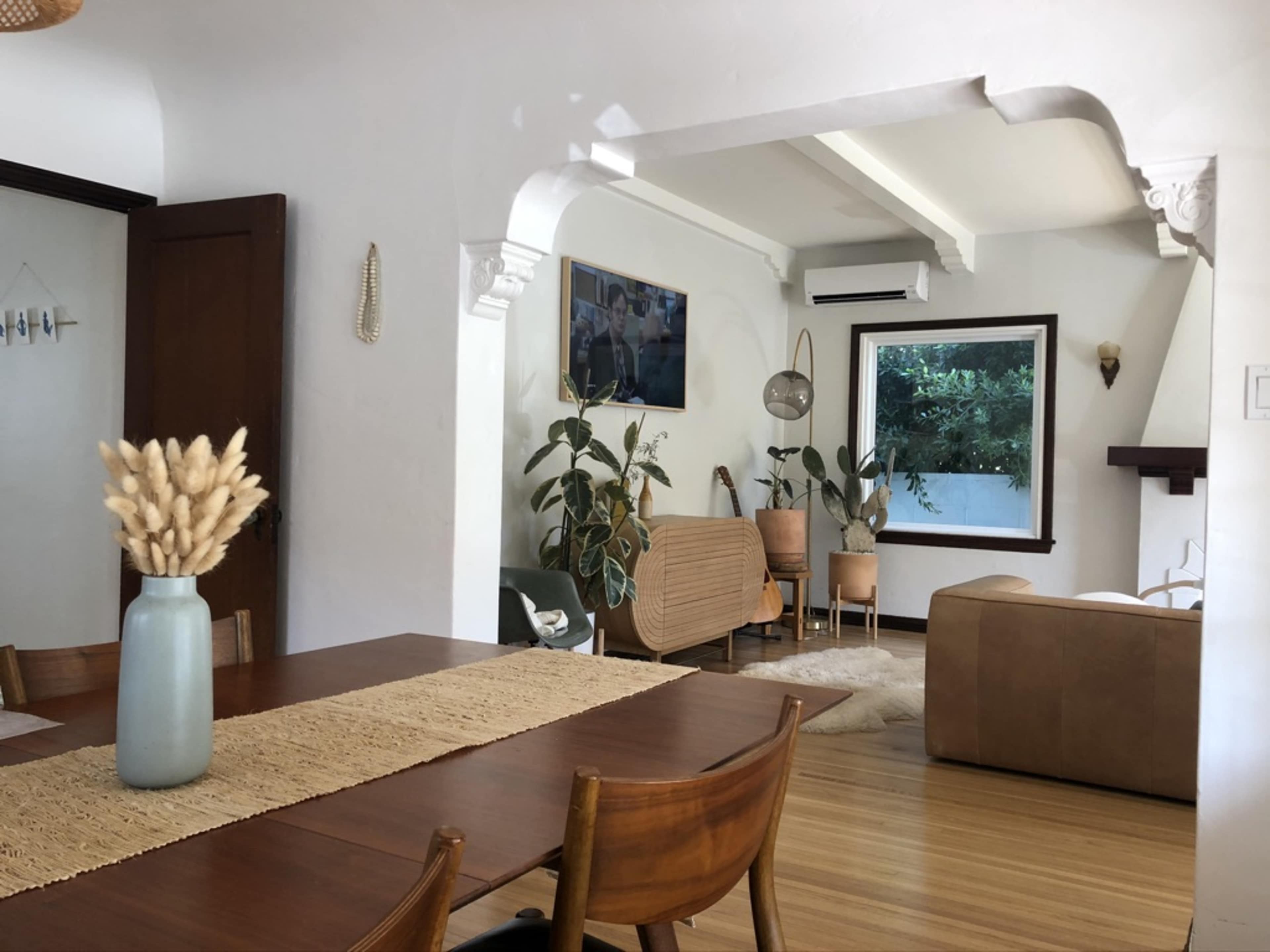 A bright, open living space featuring a dining table, chairs, and a cozy seating area with plants and decorative elements.