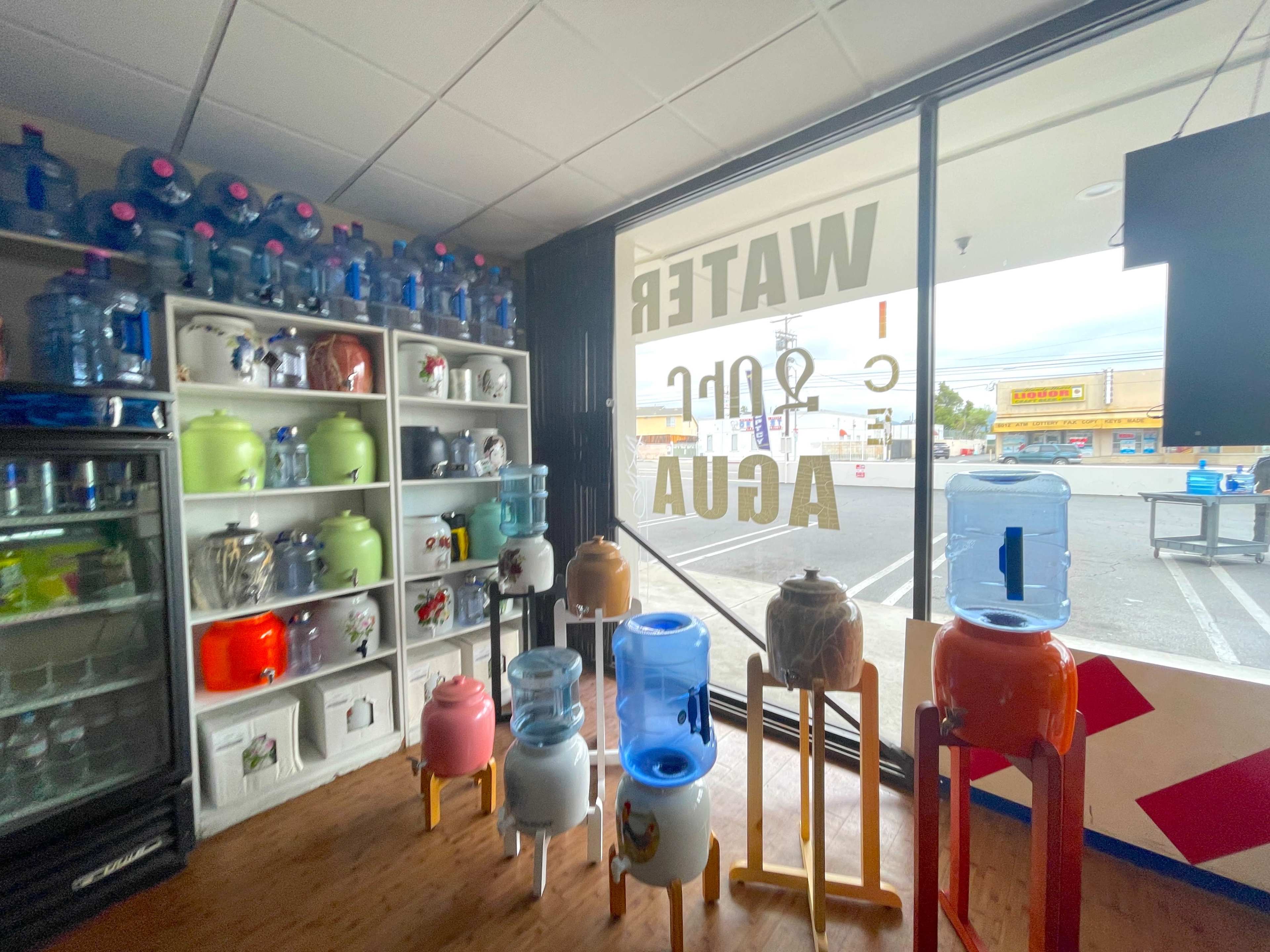 The image shows a storefront with various water dispensers displayed, along with shelves filled with water containers and a large sign indicating "WATER."