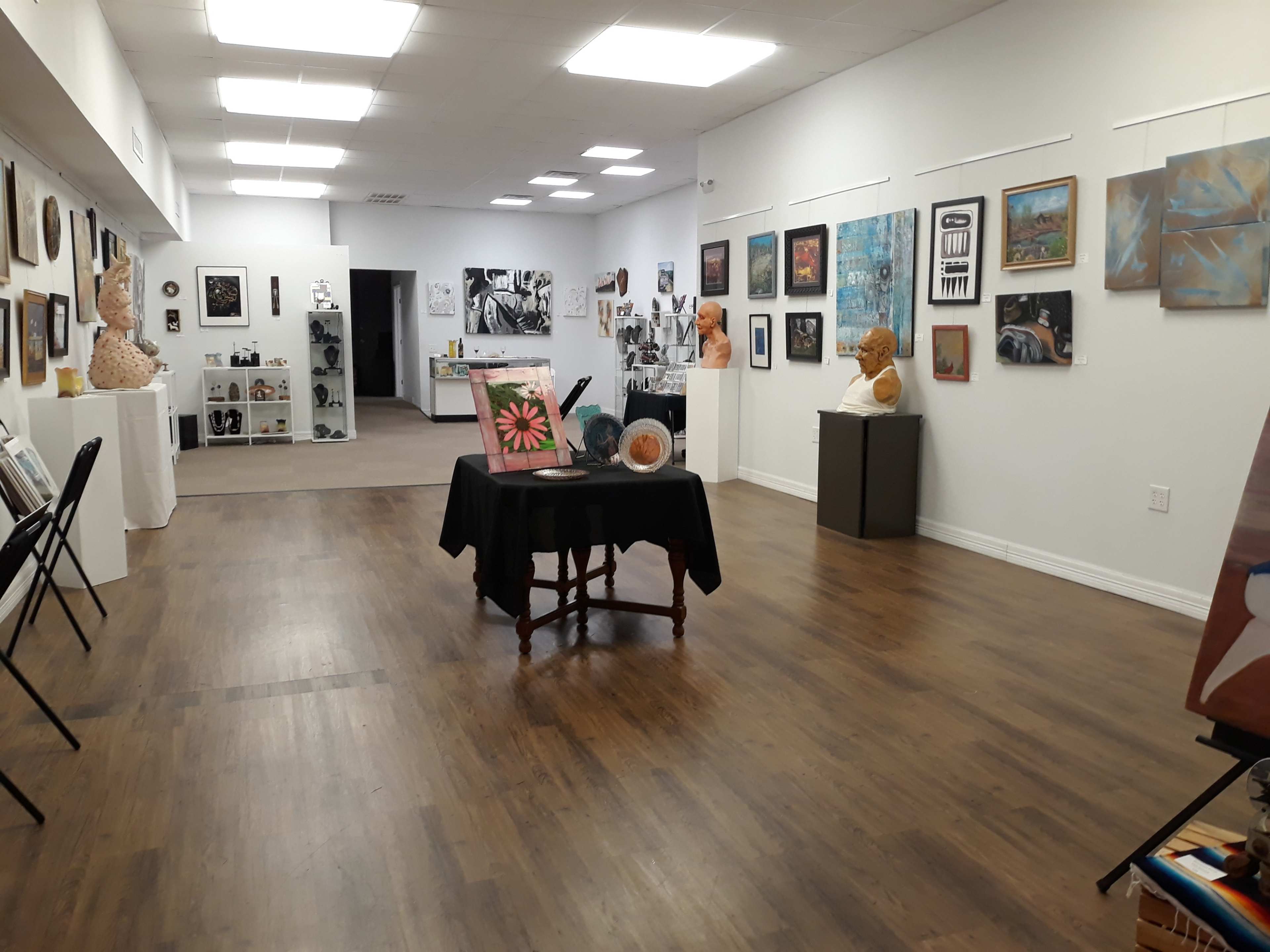 The image shows an art gallery interior with various artworks displayed on the walls and sculptures placed throughout the space.