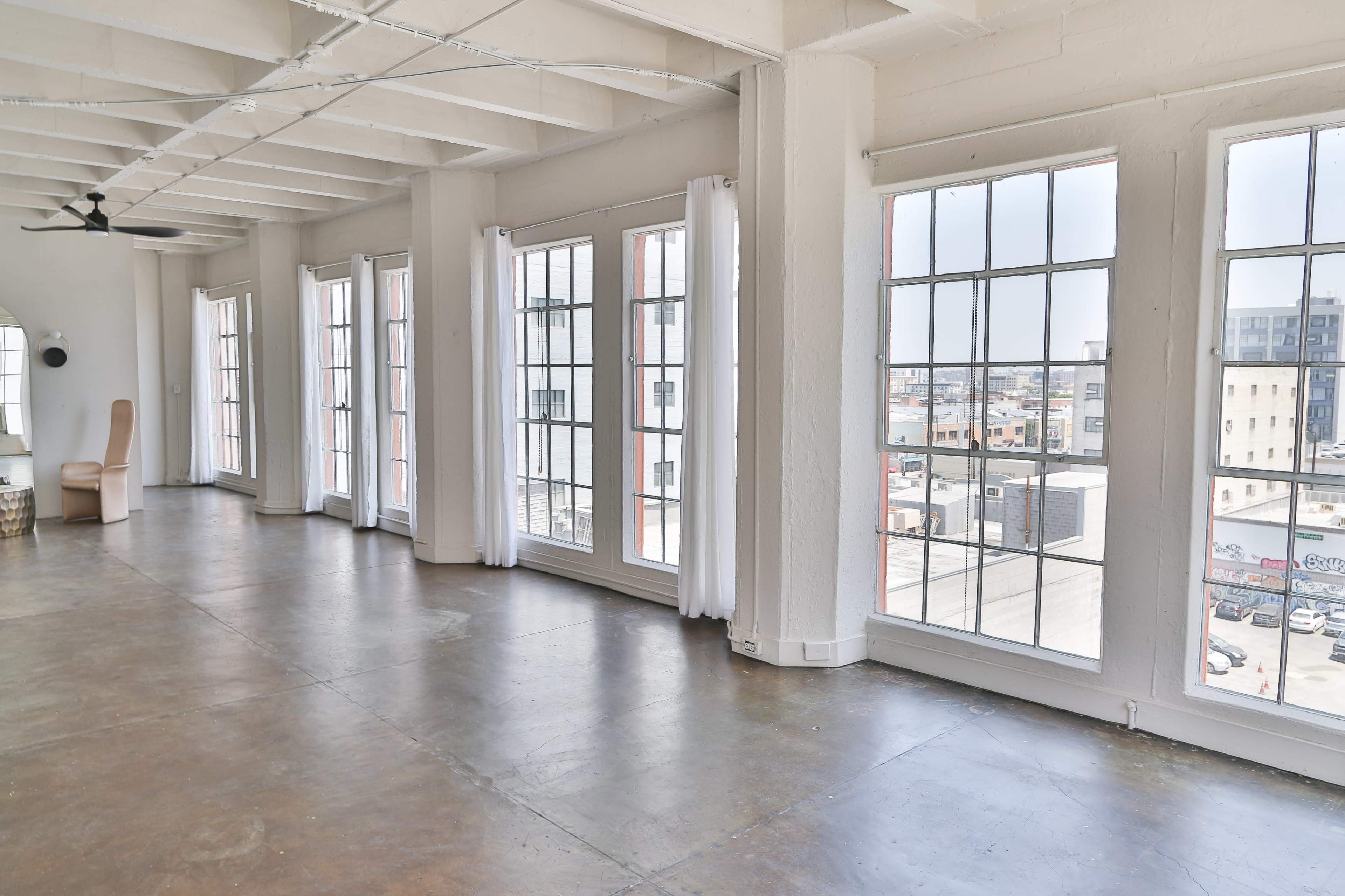A spacious, well-lit room with large windows and polished concrete flooring, overlooking an urban landscape.