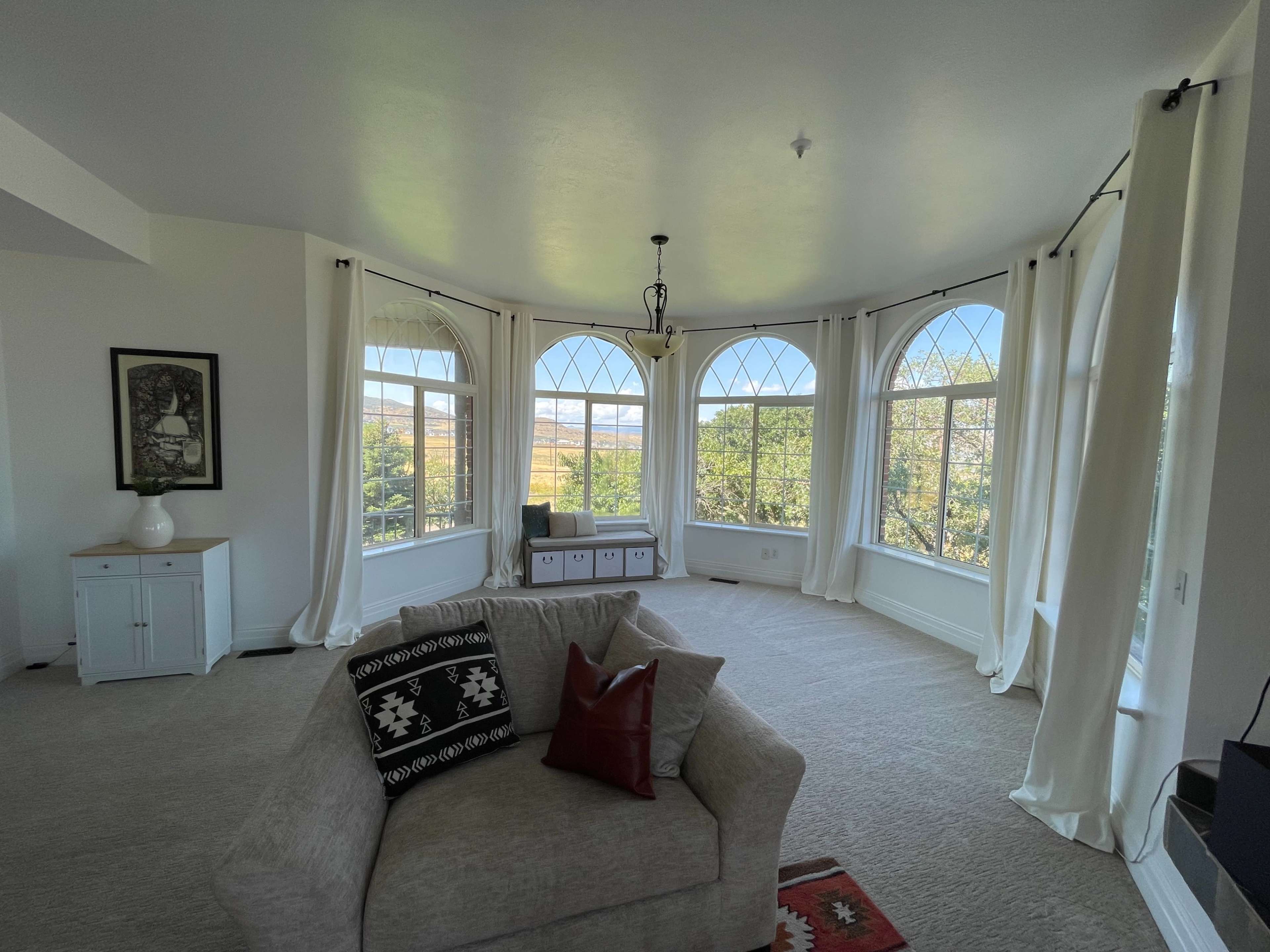 A spacious living room features large windows with arched designs that overlook a scenic view, accompanied by light-colored curtains and a central sofa.