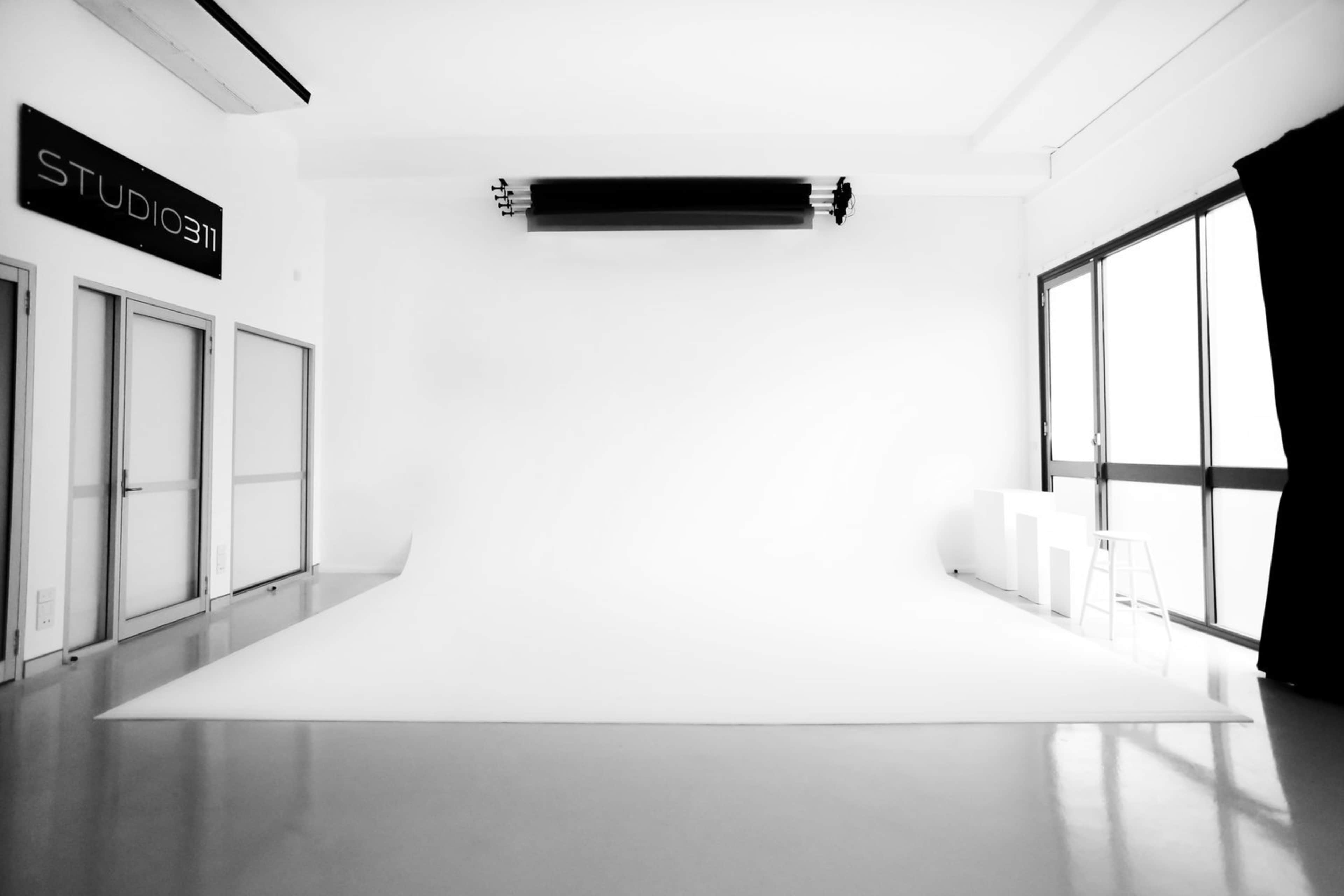 A spacious, minimalist photography studio with a white backdrop and large windows.