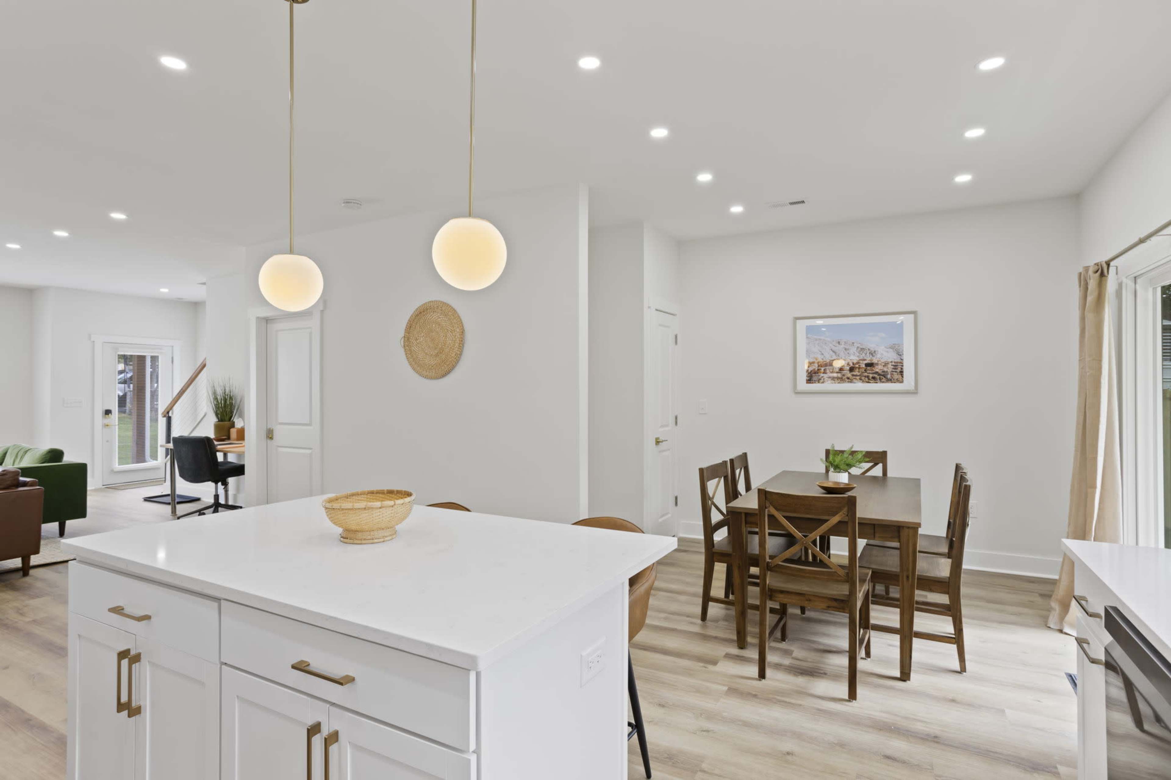 The image shows a modern kitchen and dining area with a central island, wooden dining table, and soft lighting.