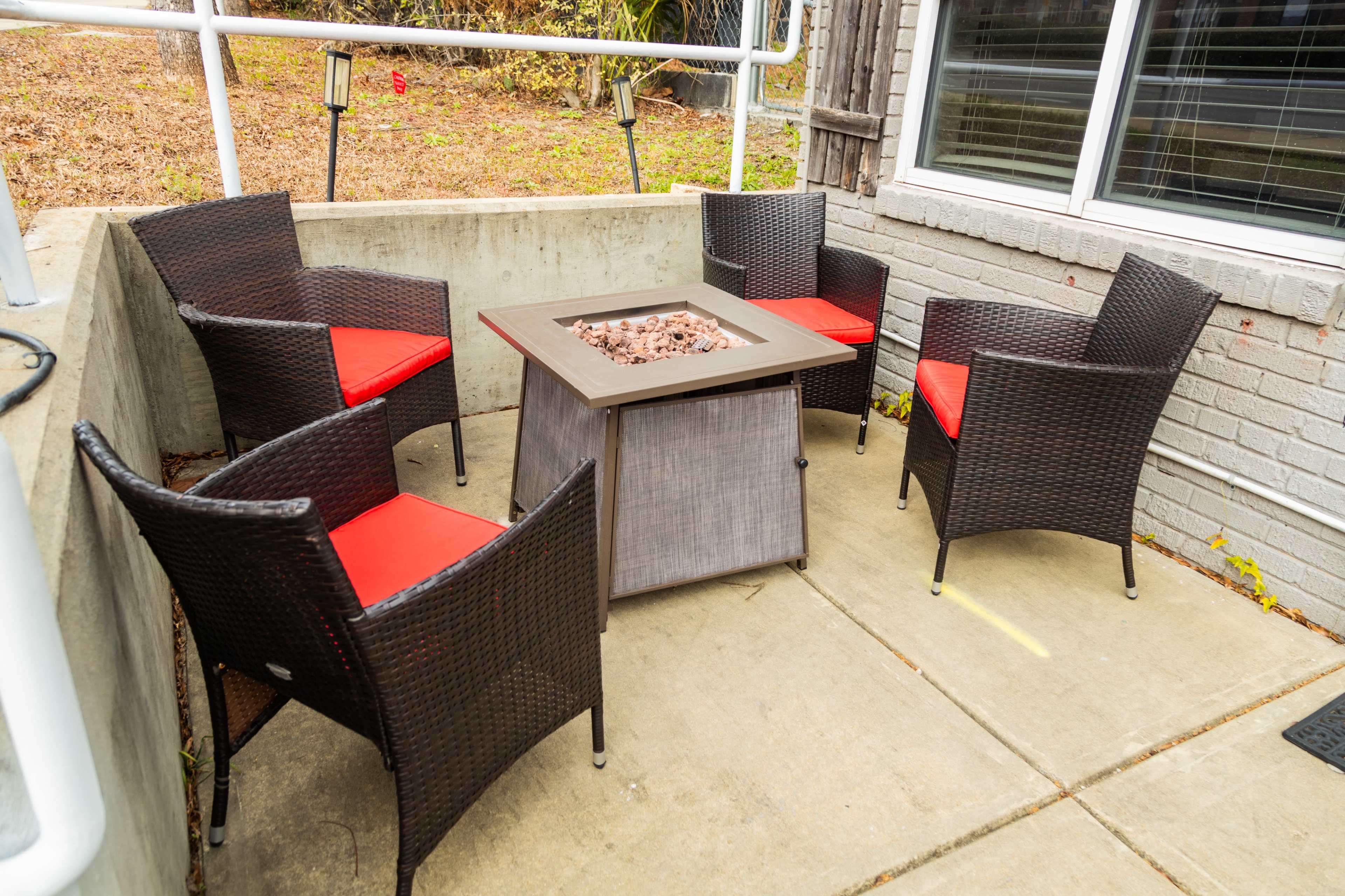 A seating area features four wicker chairs with red cushions arranged around a square fire pit.
