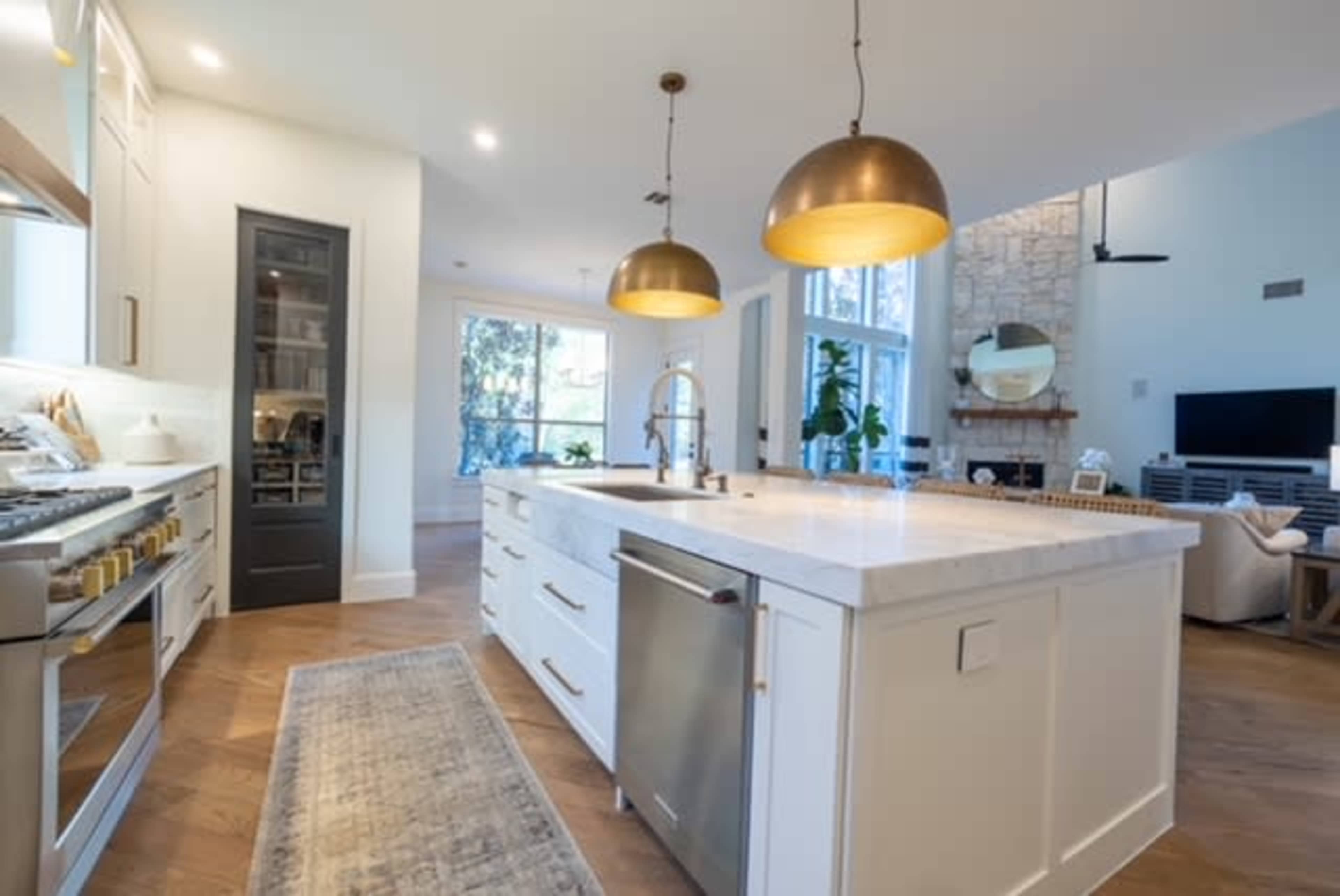 A modern kitchen featuring a central island with a marble countertop, gold pendant lights overhead, and stainless steel appliances.