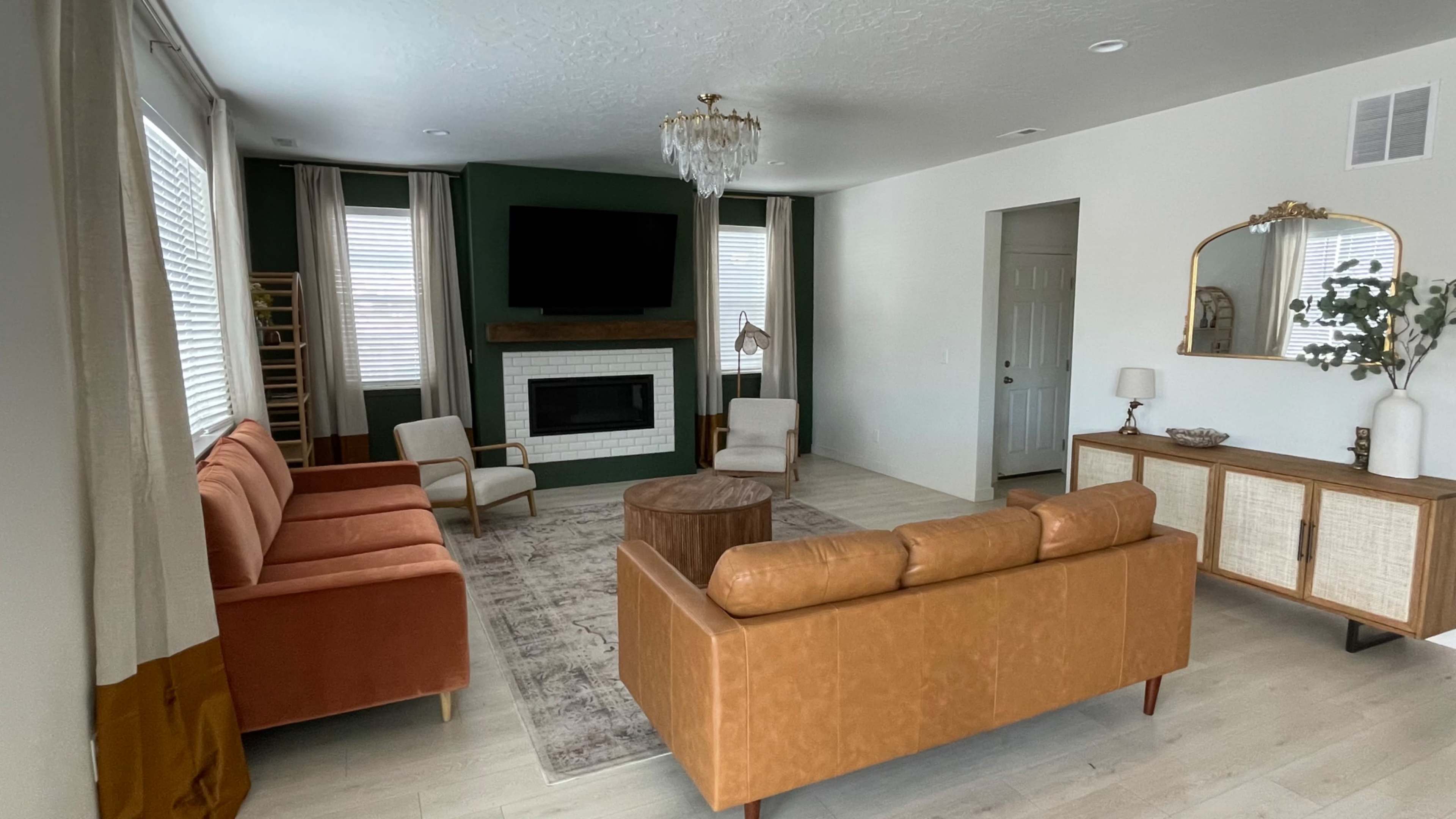 The living room features a combination of orange and brown sofas, a fireplace with a TV above it, and large windows with light curtains.