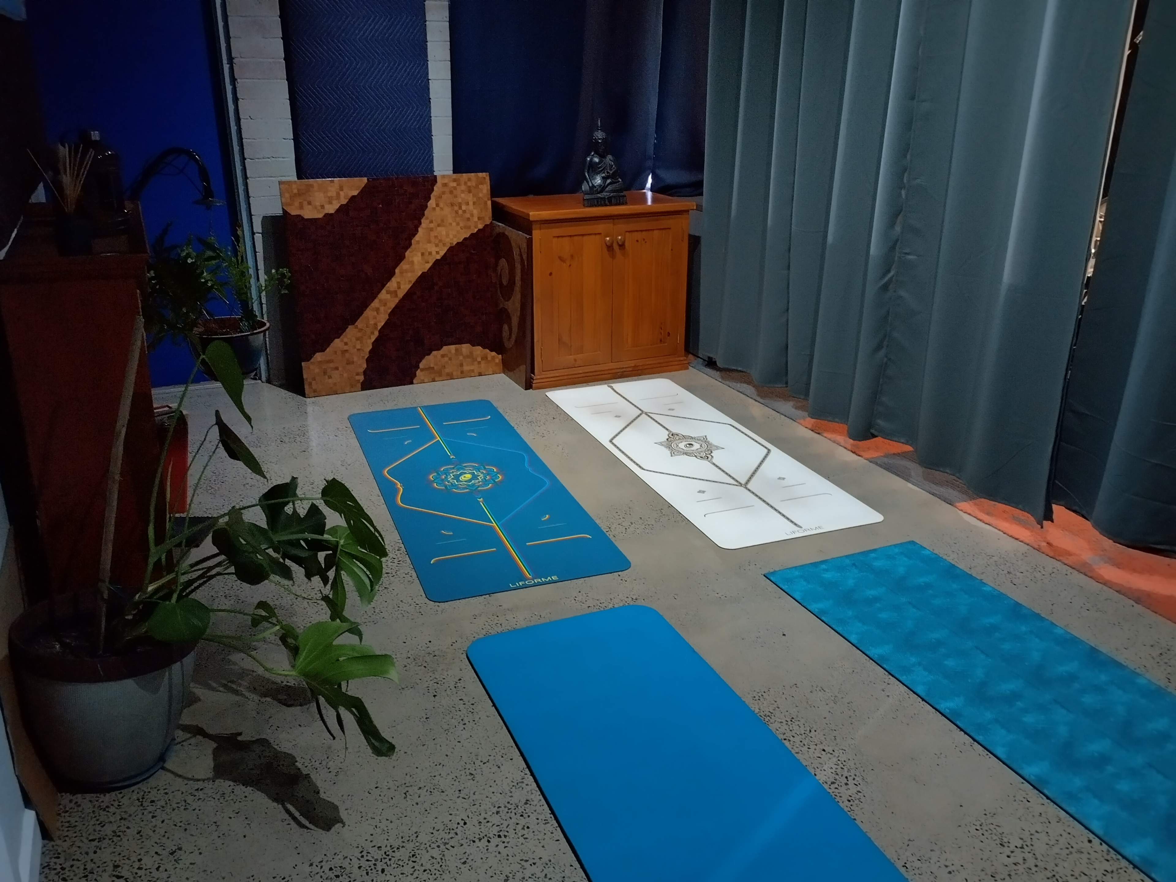 A serene indoor space with five yoga mats arranged neatly on a concrete floor, accompanied by a wooden cabinet and potted plants.
