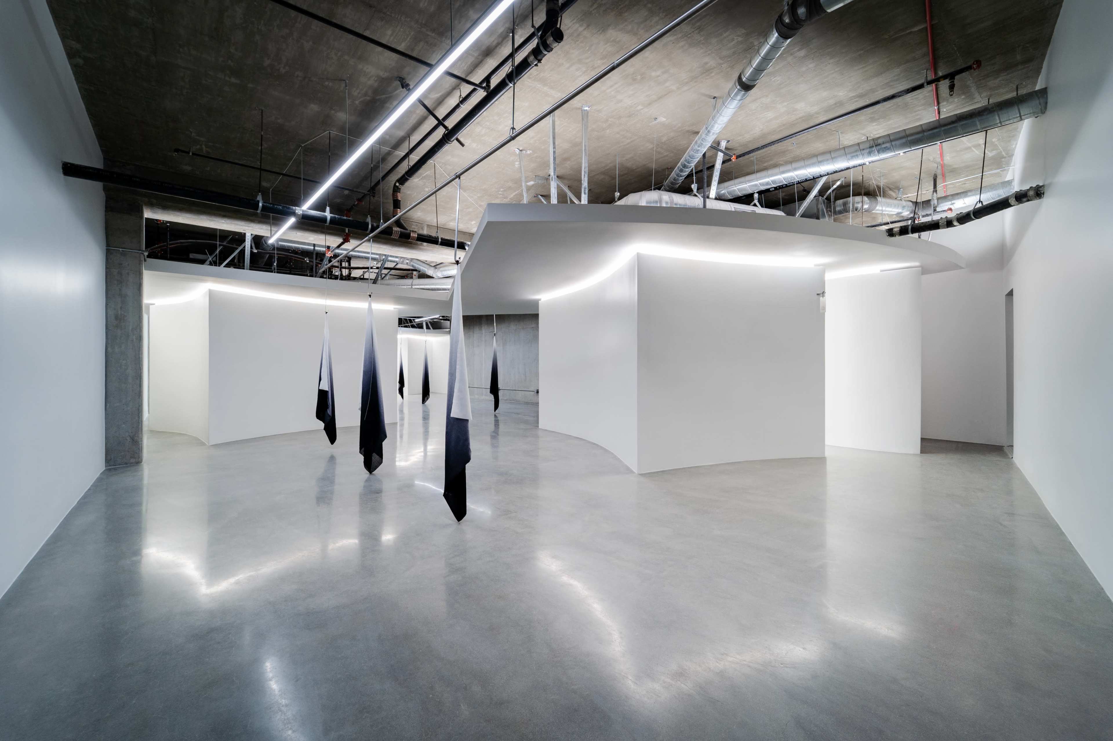 The image shows an interior space with smooth, curved walls, polished concrete flooring, and black and white hanging fabric installations.