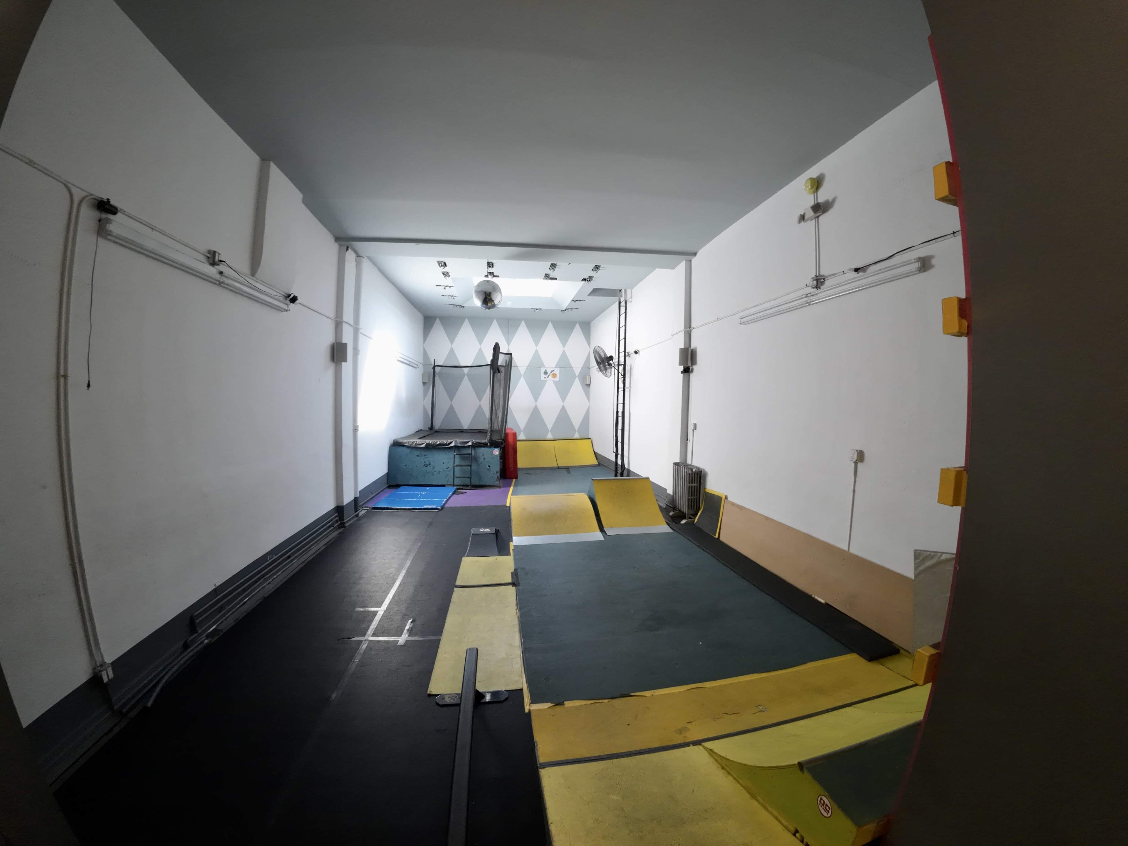 The image shows a small indoor space designed for parkour training, featuring ramps, mats, and a colorful geometric wall.