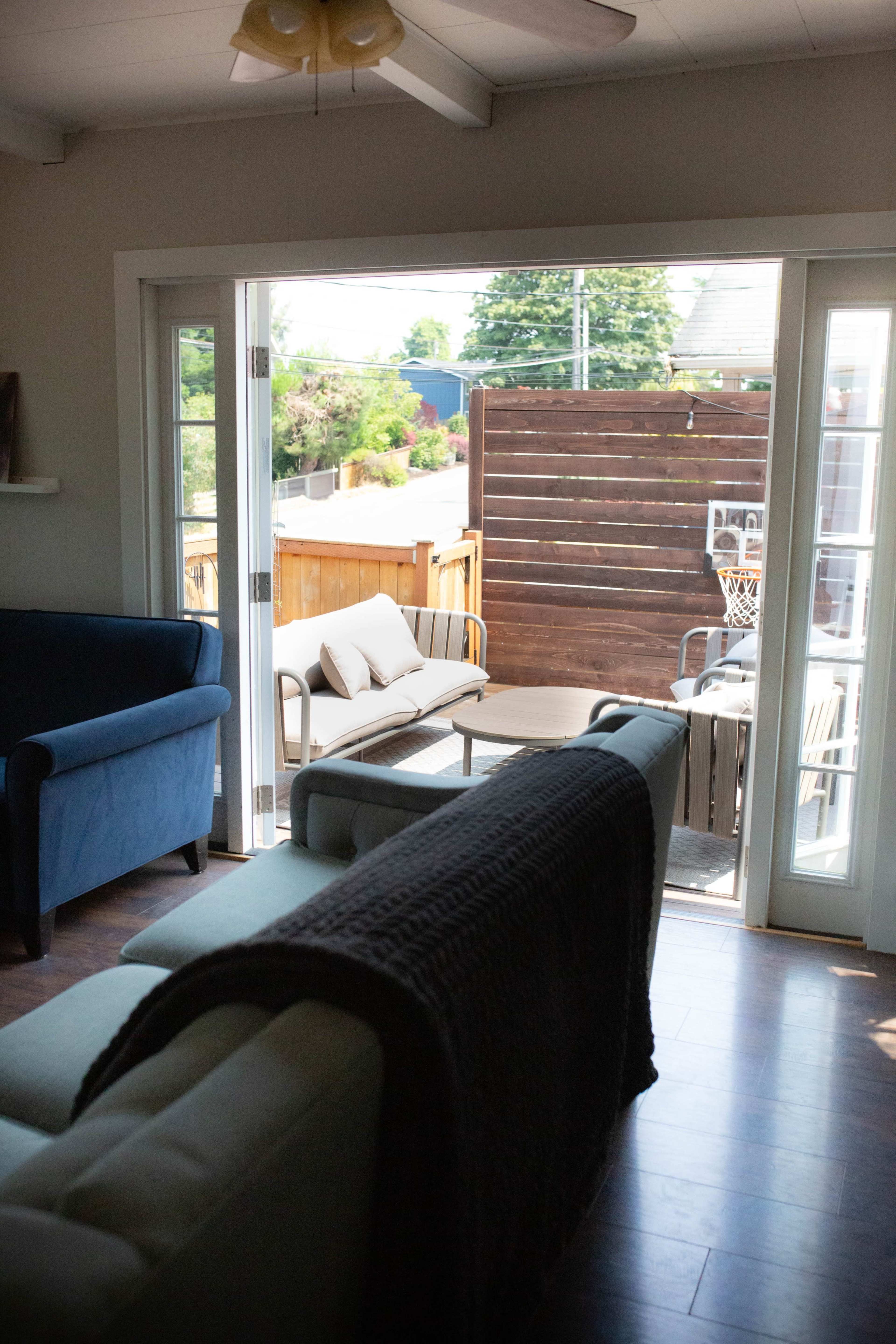 The image shows a living room with two couches, a view of an outdoor patio through glass doors, and a wooden fence in the background.