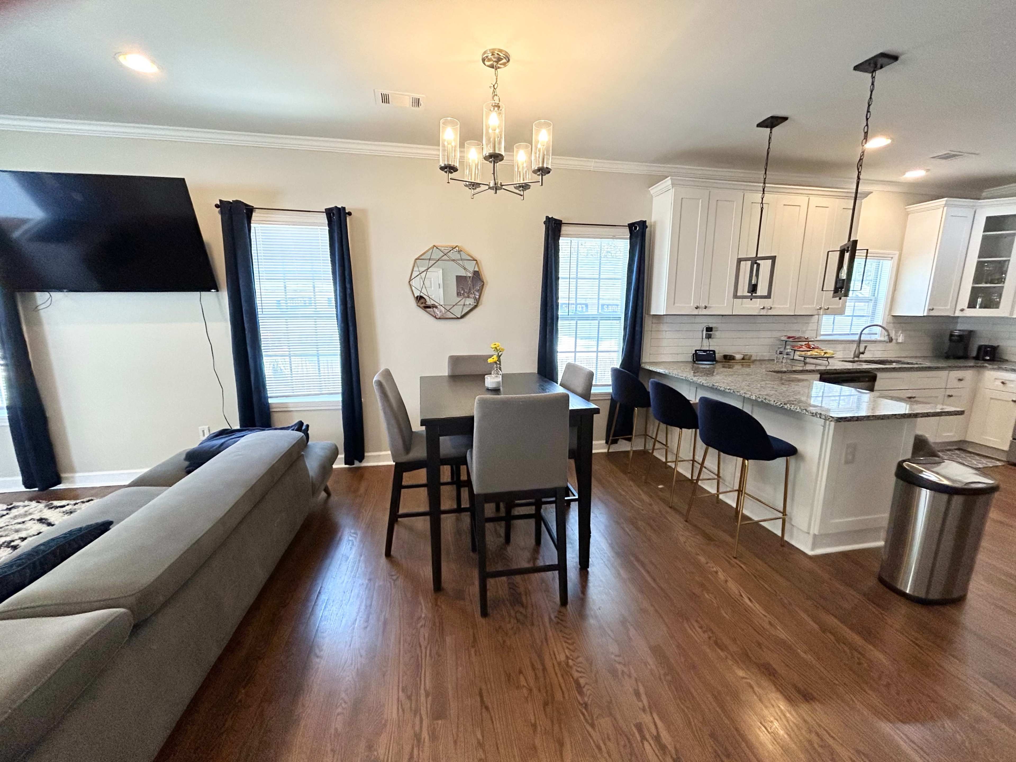 The image shows a modern open-concept living and dining area with a table, chairs, and a well-equipped kitchen.