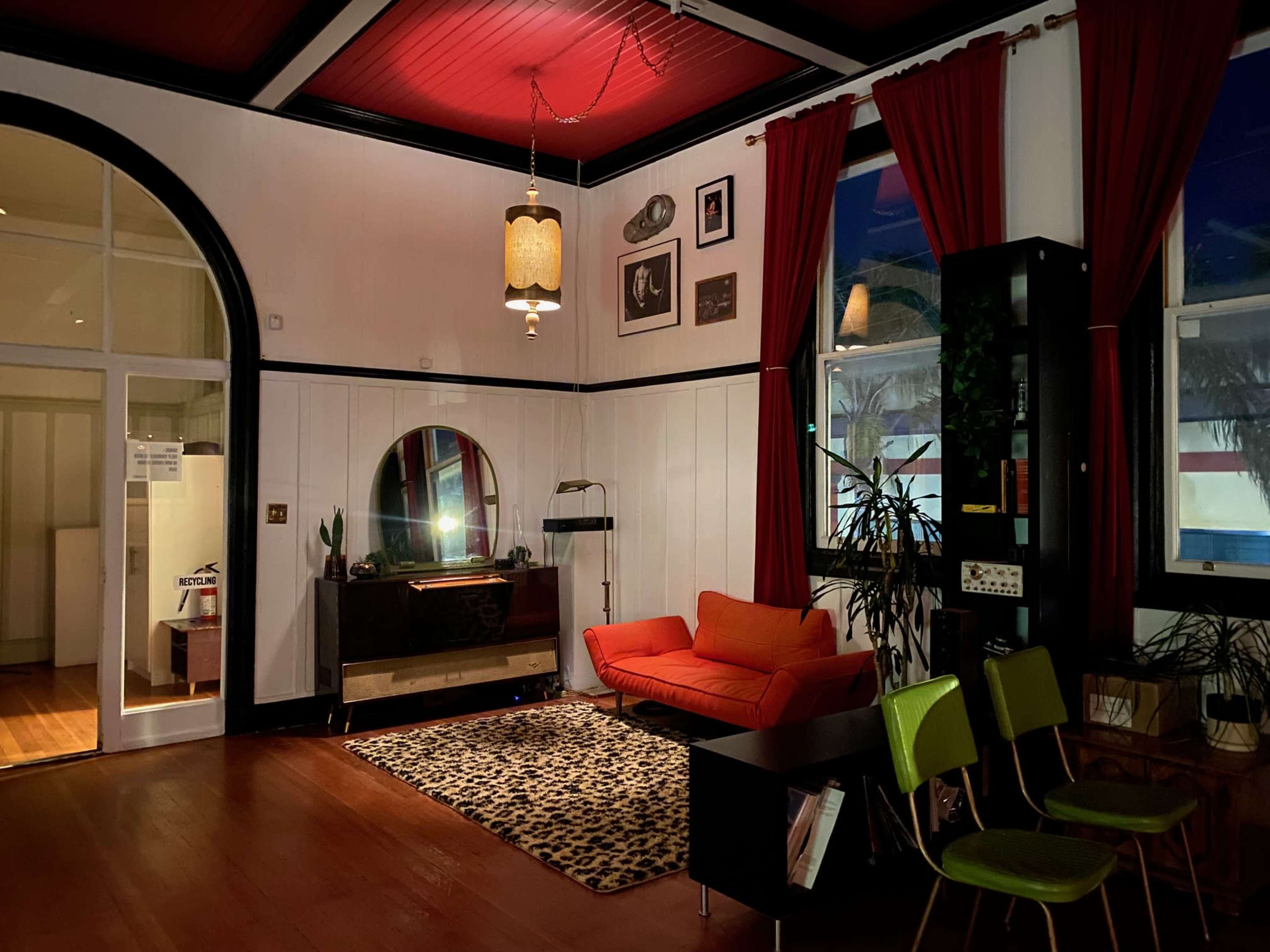 The room features a red ceiling, an orange sofa, and a leopard-print rug, with a large mirror and potted plants creating a cozy atmosphere.
