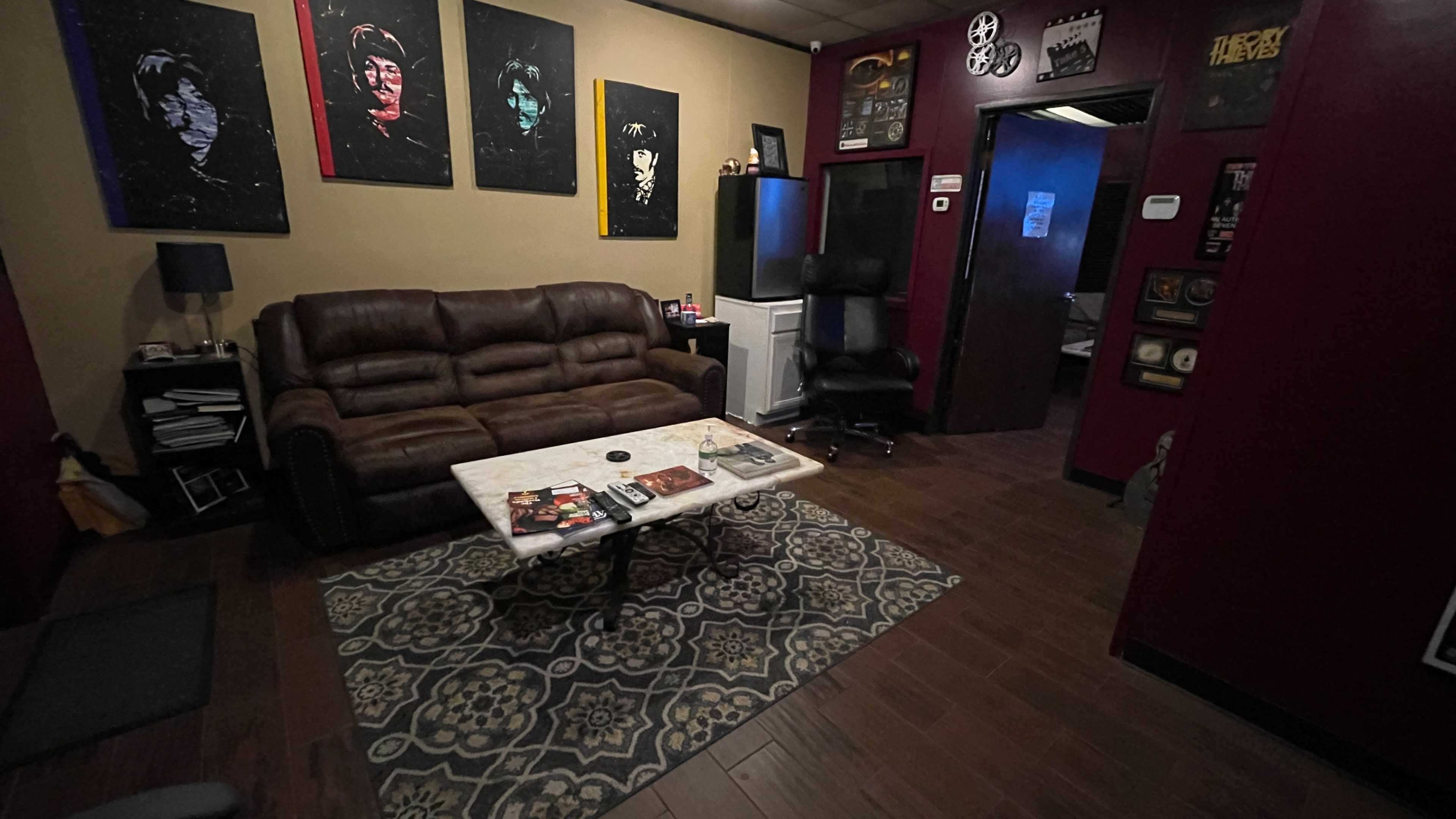 The room features a brown leather couch, a marble coffee table with magazines on it, and walls adorned with framed artwork, leading to a doorway on the right.