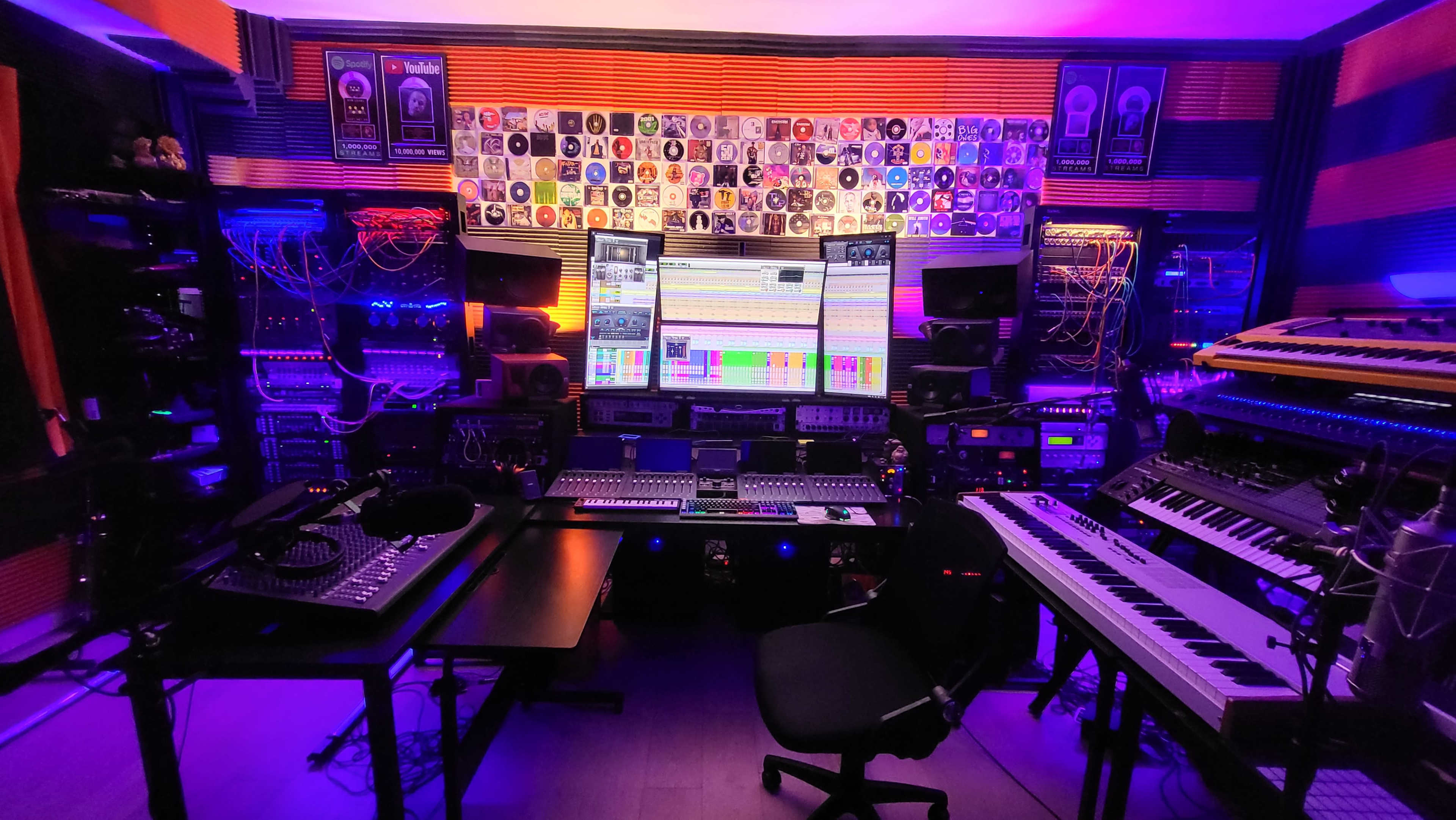 The image shows a music production studio with multiple audio equipment, a large screen displaying tracks, and colorful LED lighting.