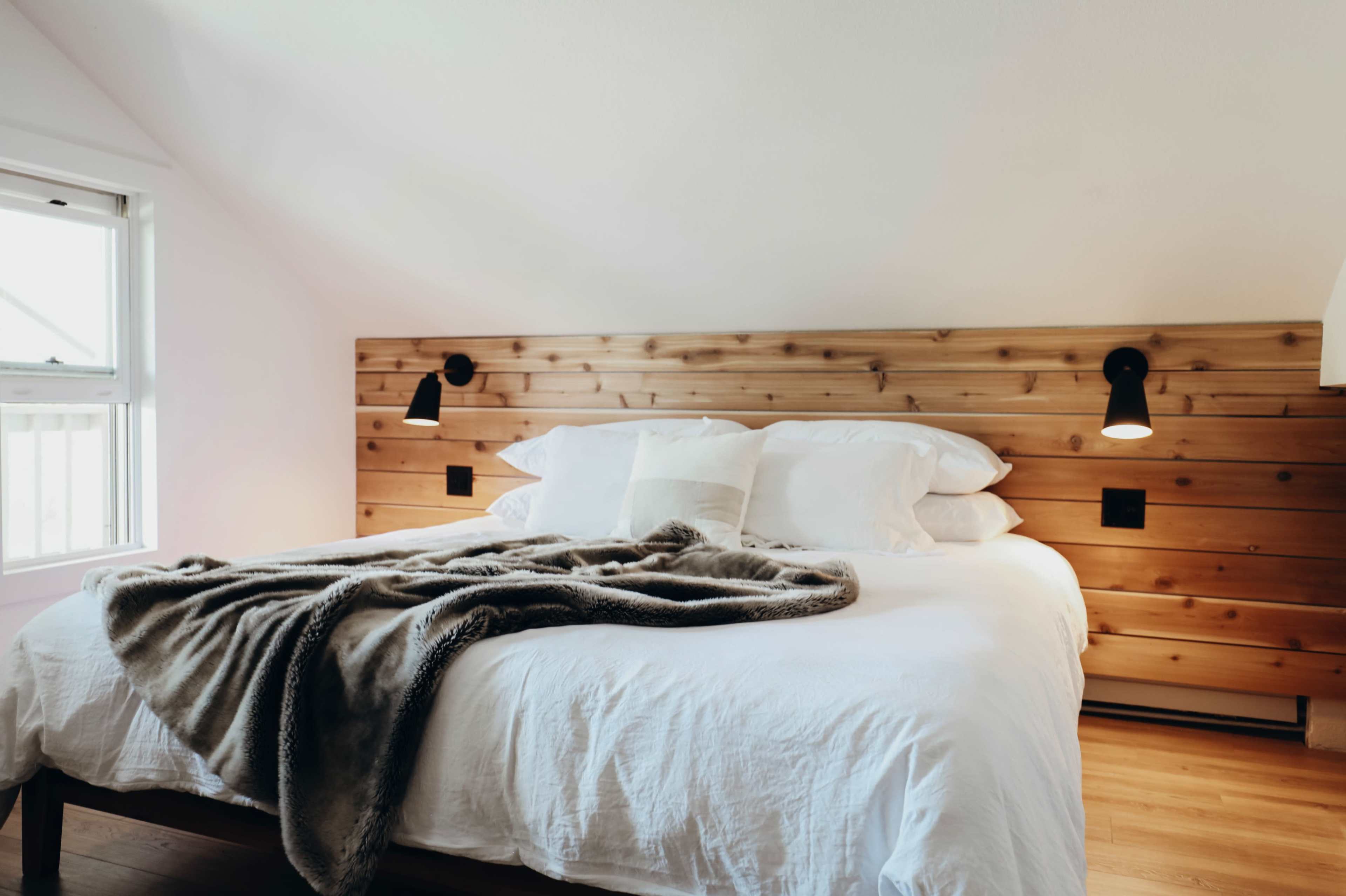A cozy bedroom with a wooden headboard, a neatly made bed topped with white linens, and a soft blanket draped over it.