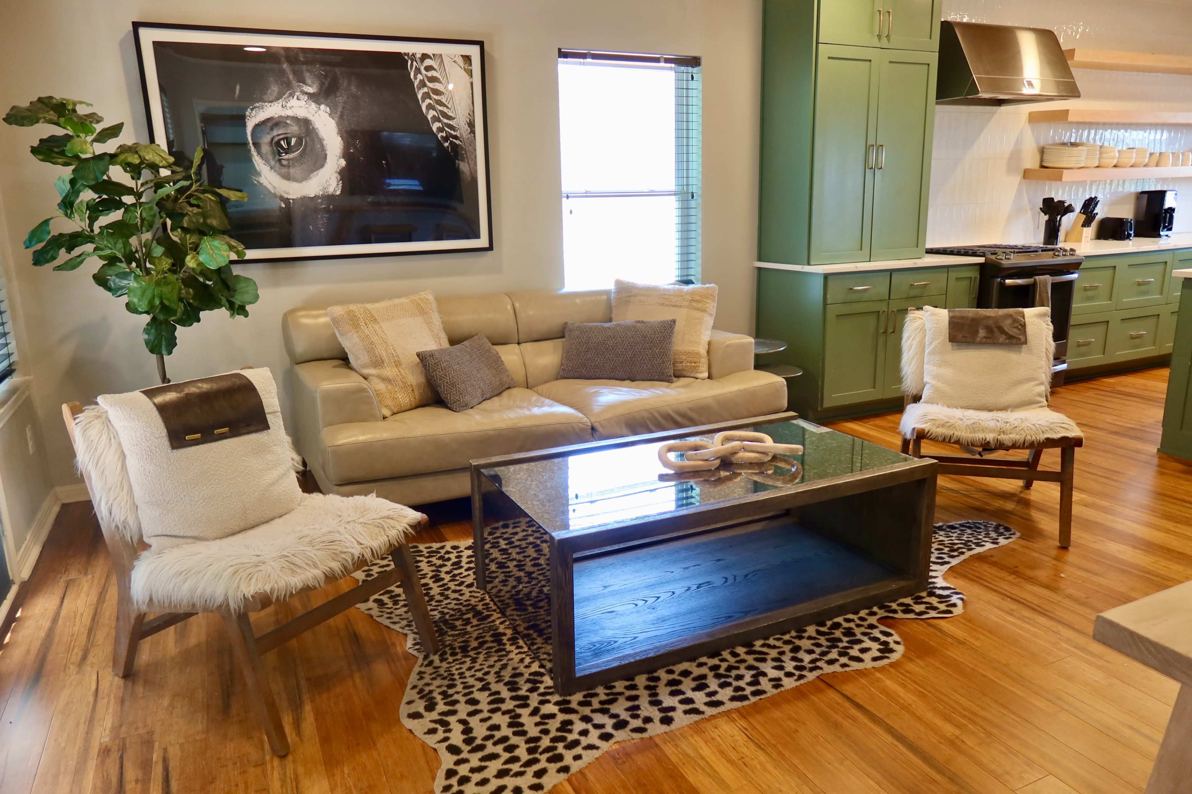 The image shows a modern living room with a beige sofa, two white armchairs with textured throws, a wooden coffee table, and a decorative area rug on a wooden floor.