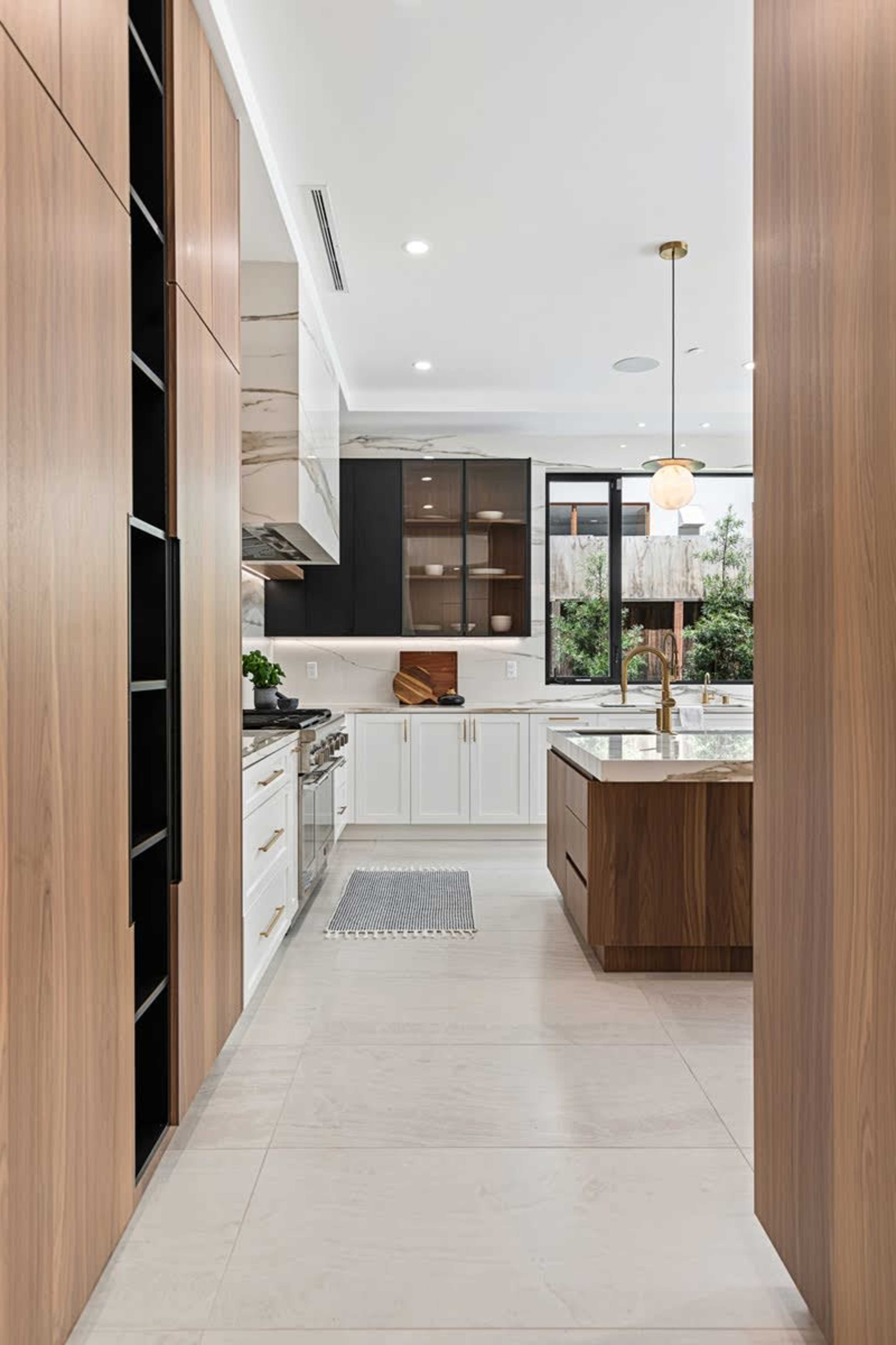 A modern kitchen featuring wood cabinetry, a central island with a marble countertop, and large windows that allow natural light to fill the space.