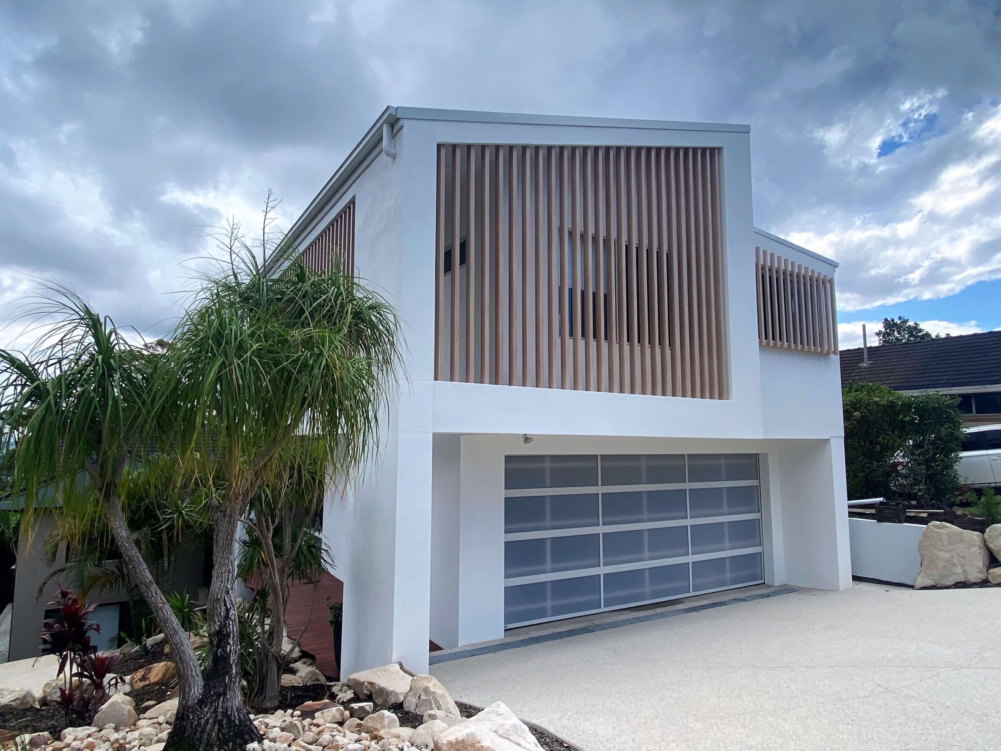 A modern house with vertical wooden slats and a large garage door is set against a cloudy sky.