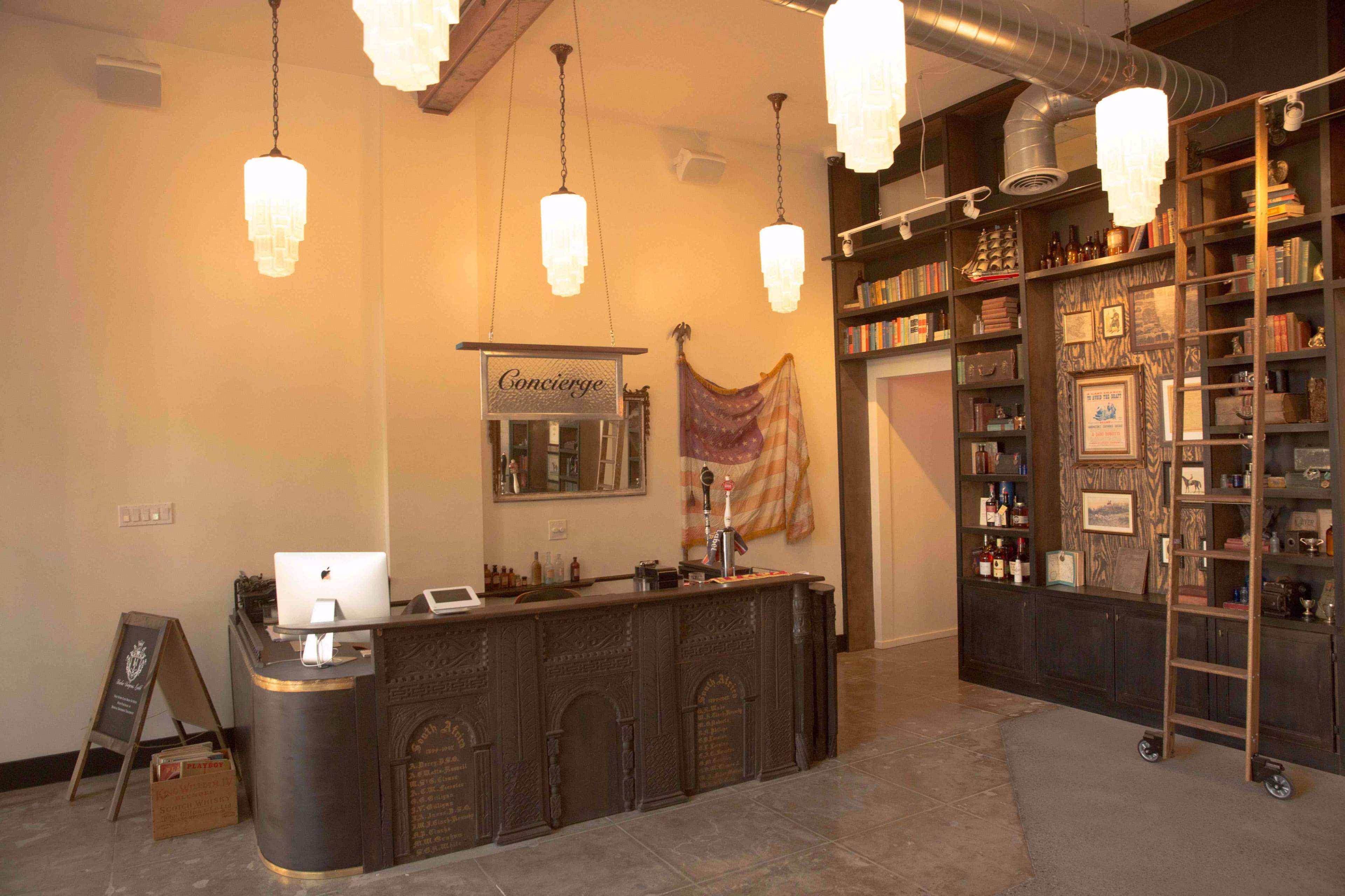 The image depicts a modern concierge desk with a computer and decorative shelving filled with various items, set in a well-lit interior space.