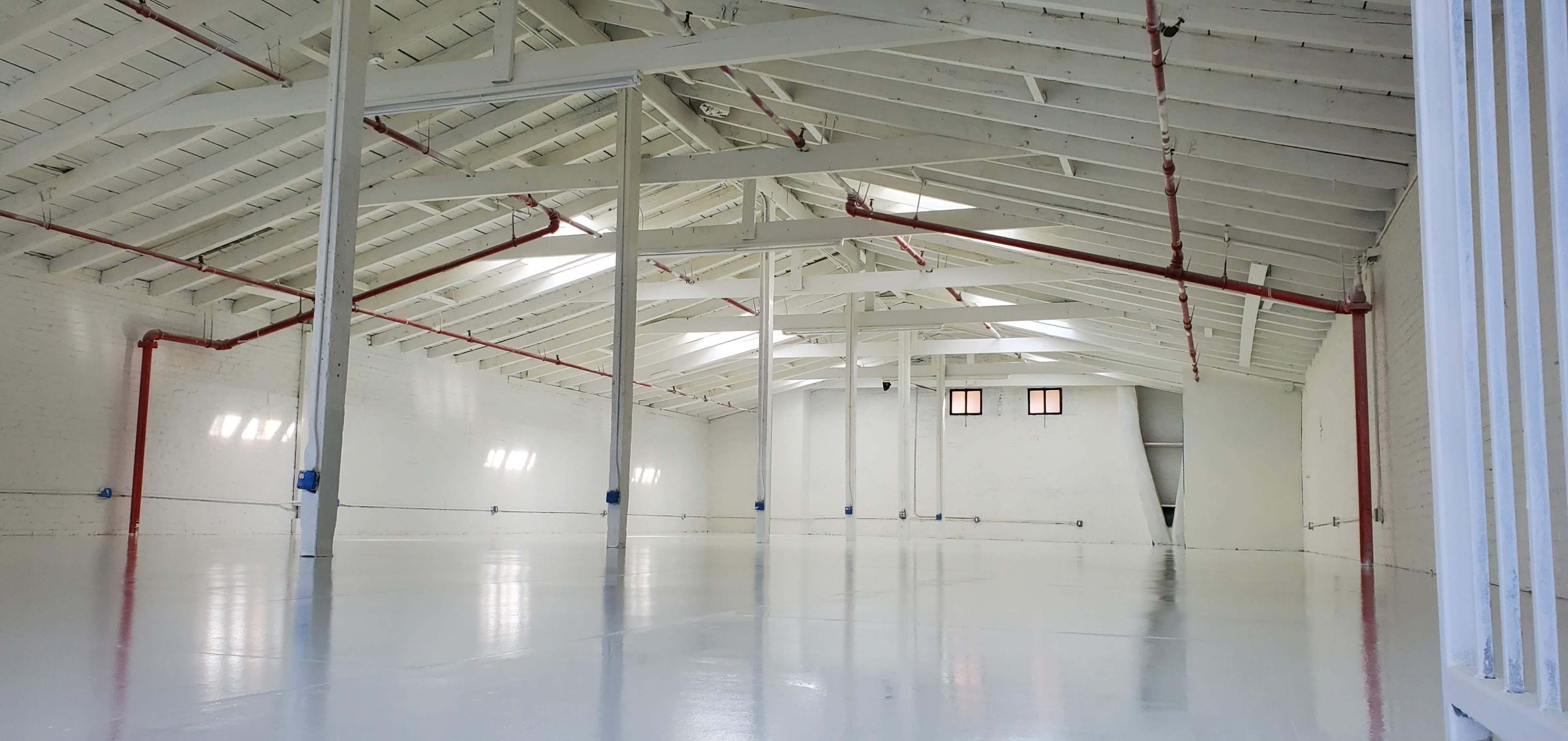 A spacious, empty warehouse with a high ceiling and bright, white walls.